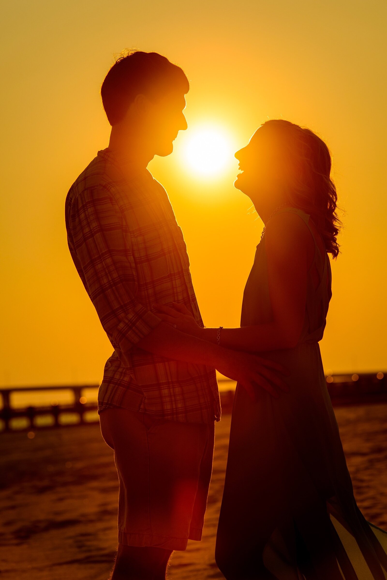 Engagement portrait on the beach, silhouette of couple with setting sun behind them