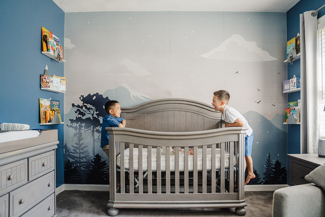 big brothers laugh at each other across new brothers crib