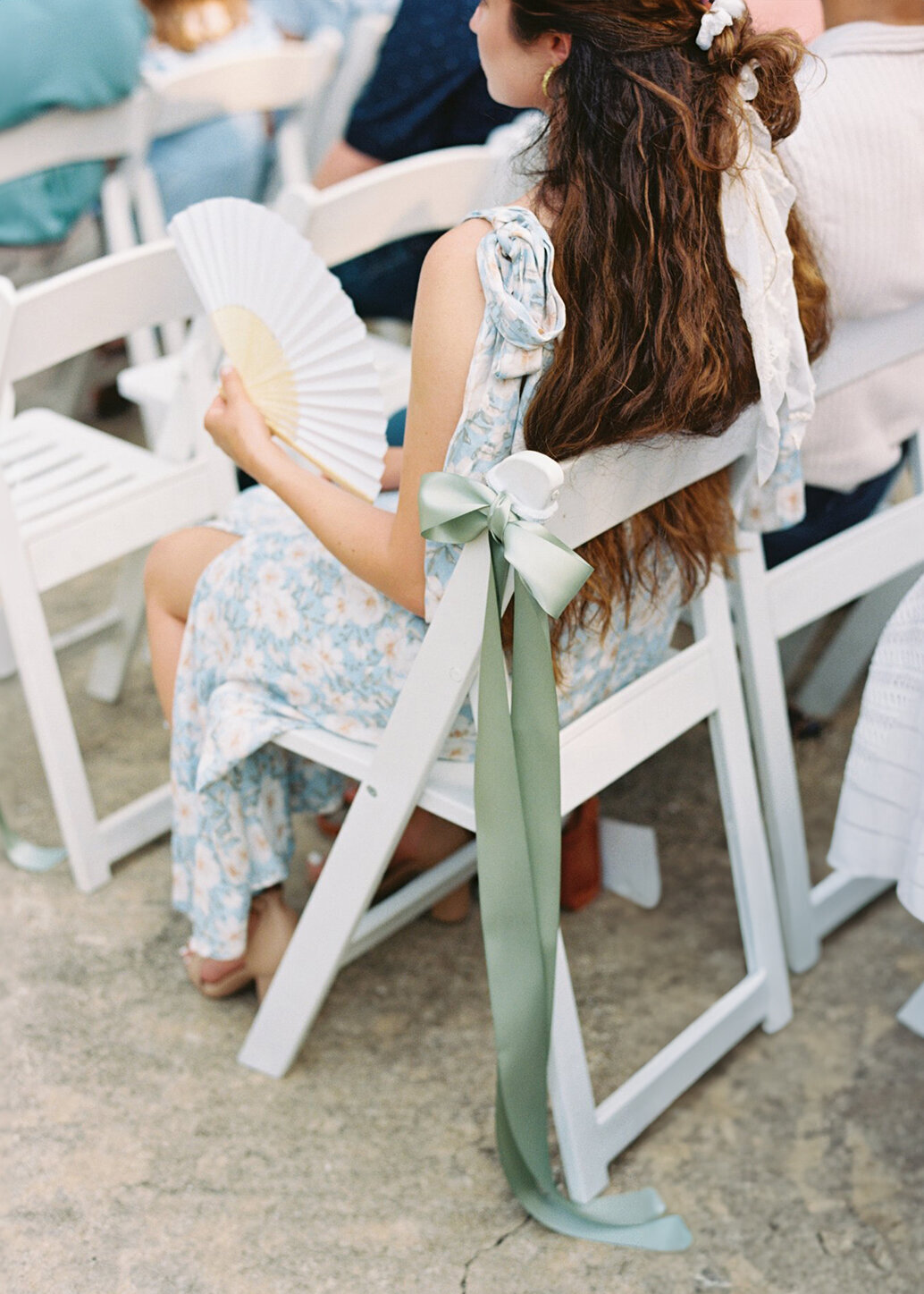 Wedding guest cooling off with custom wedding fans before the ceremony, captured on film by Morgan Alysse, Louisiana film photographer.