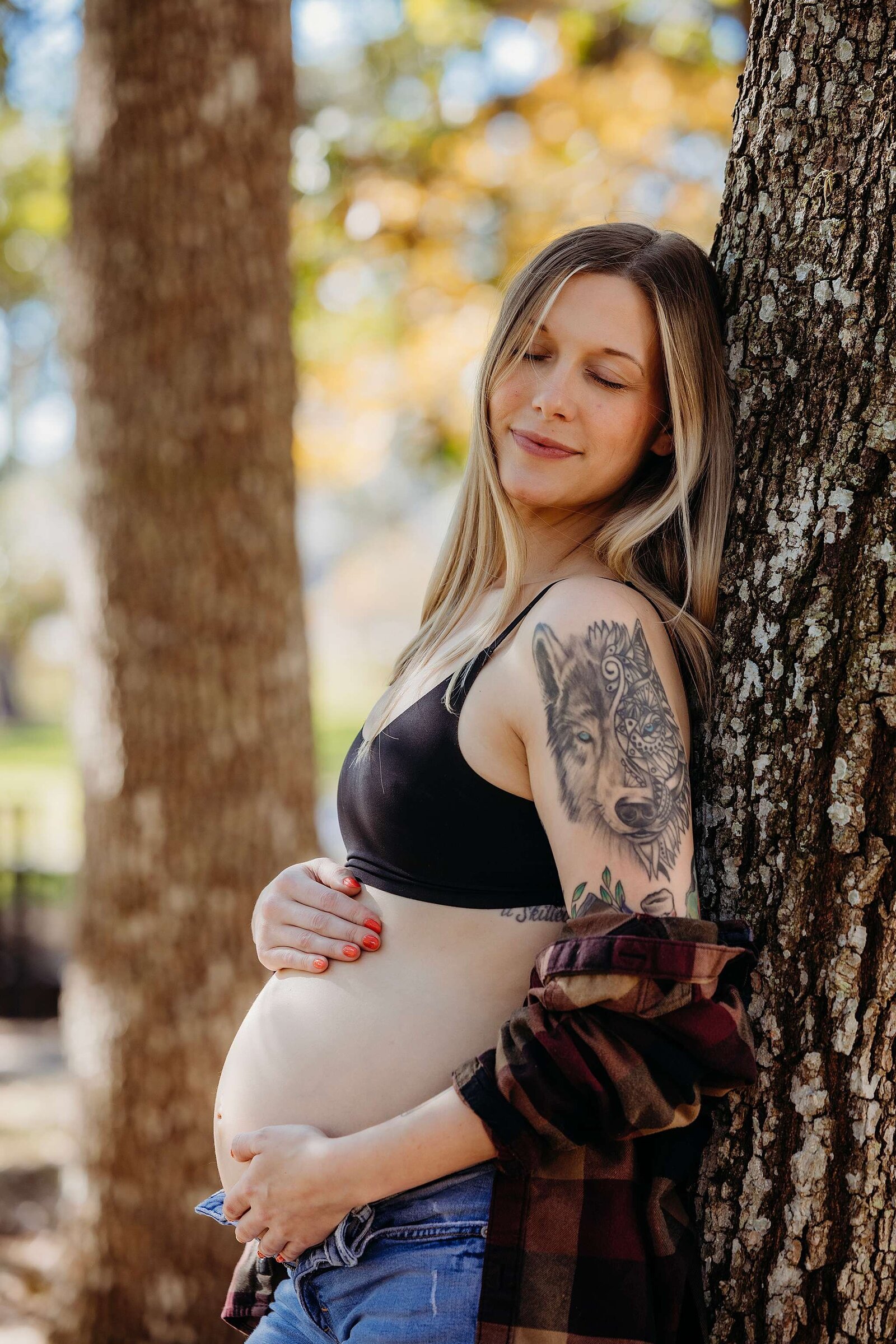 A pregnant woman with a beautiful wolf tattoo leaning against a tree during a maternity session in Orlando, Fl.