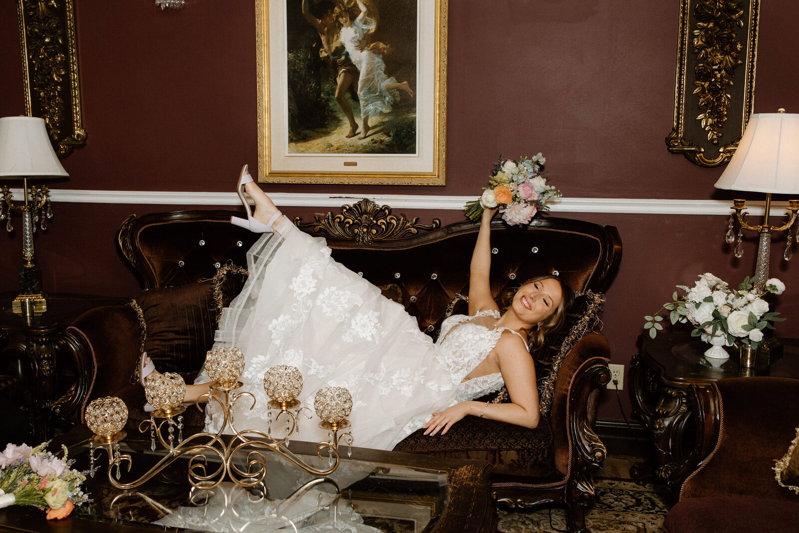 A newly married woman celebrating as she lays on a couch in her wedding dress and bouquet