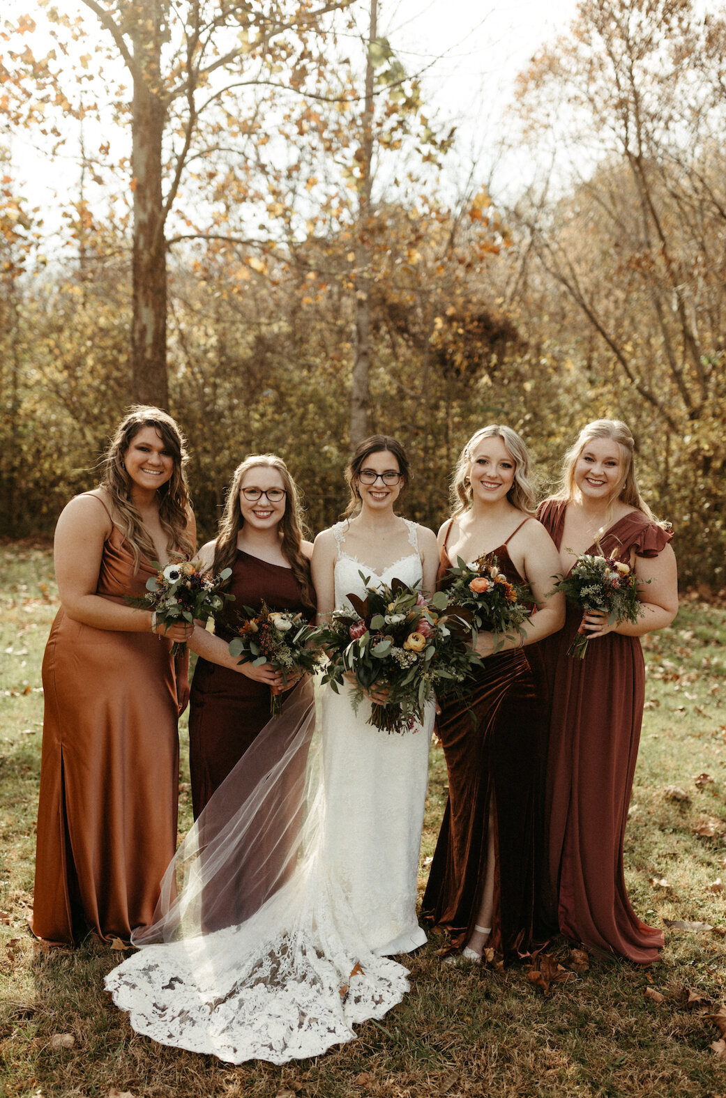 bride standing with her bridesmaids under a tree