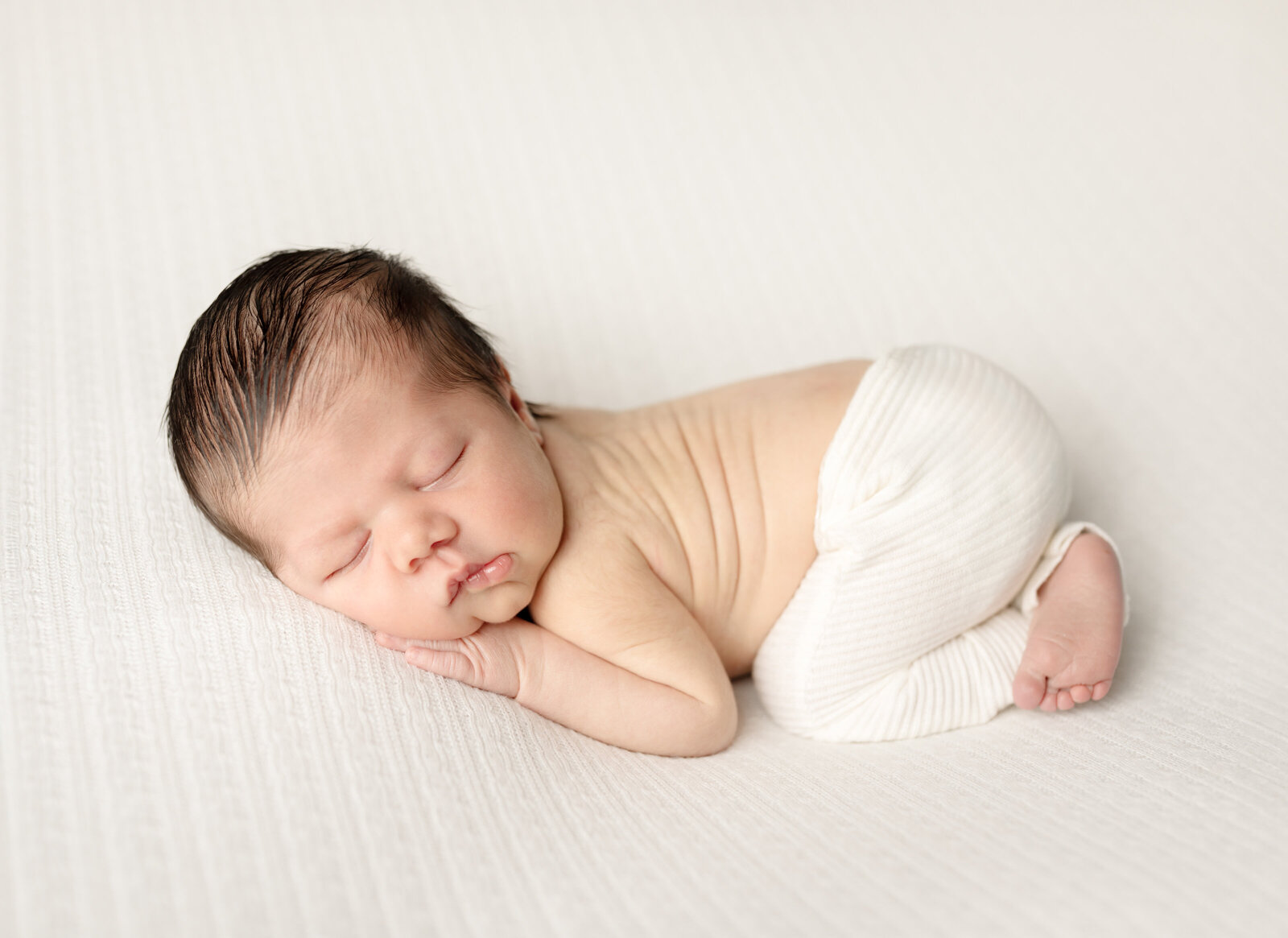 newborn baby boy in white pants posed for studio portraits