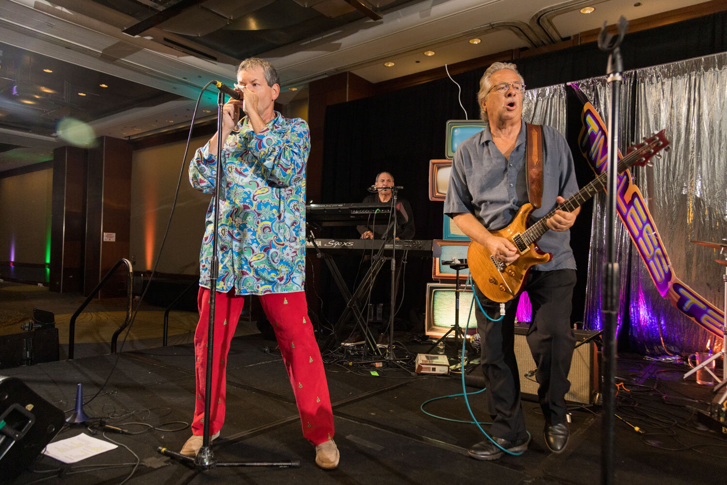 Rock band performing on stage with retro TVs in the background