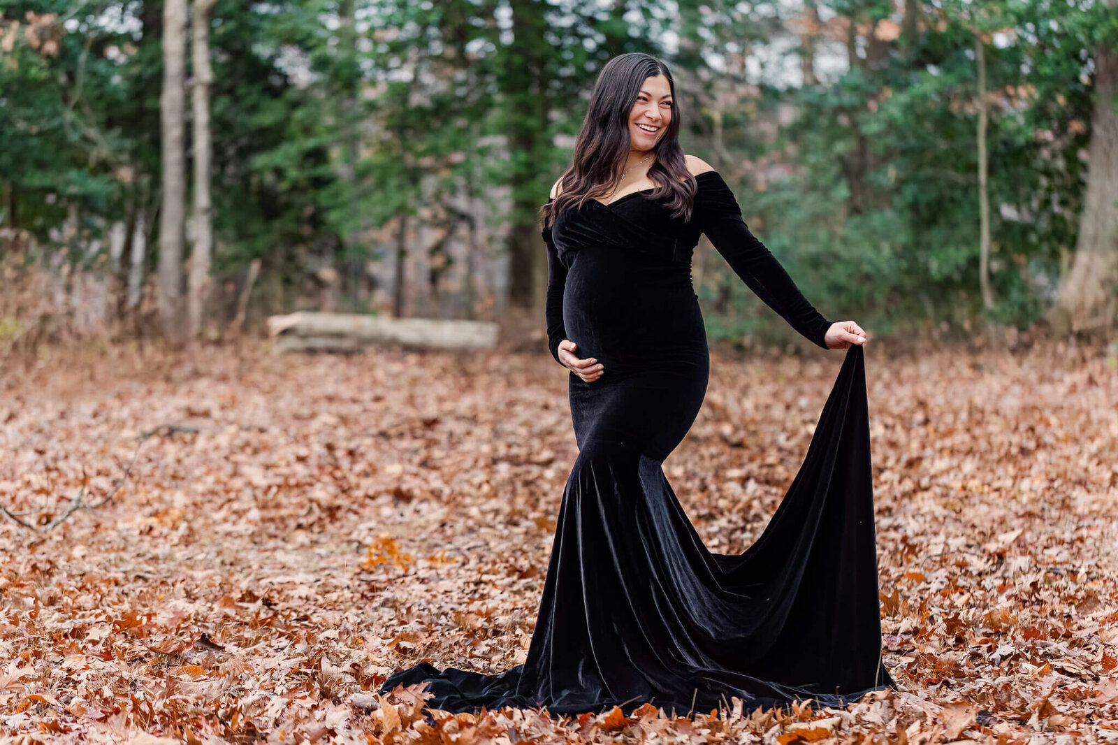 A beautiful pregnant woman in a black dress posing for her maternity portraits in a park.