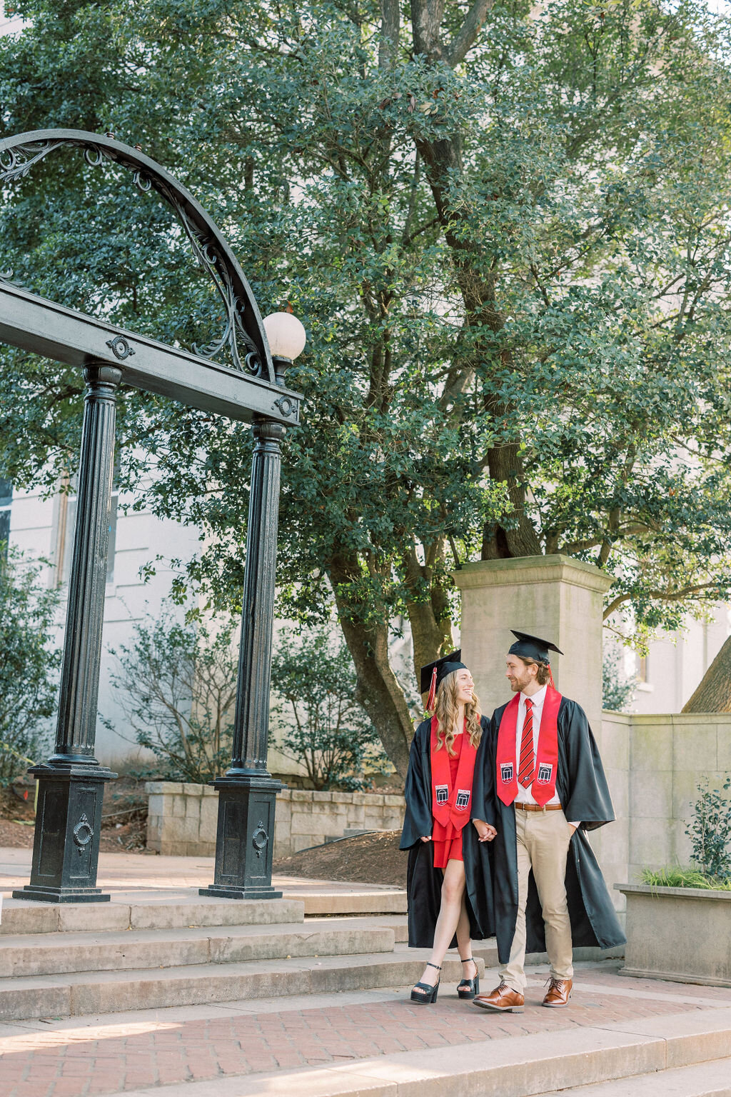 girl and guy wearing graduation robes walk under Arch at UGA