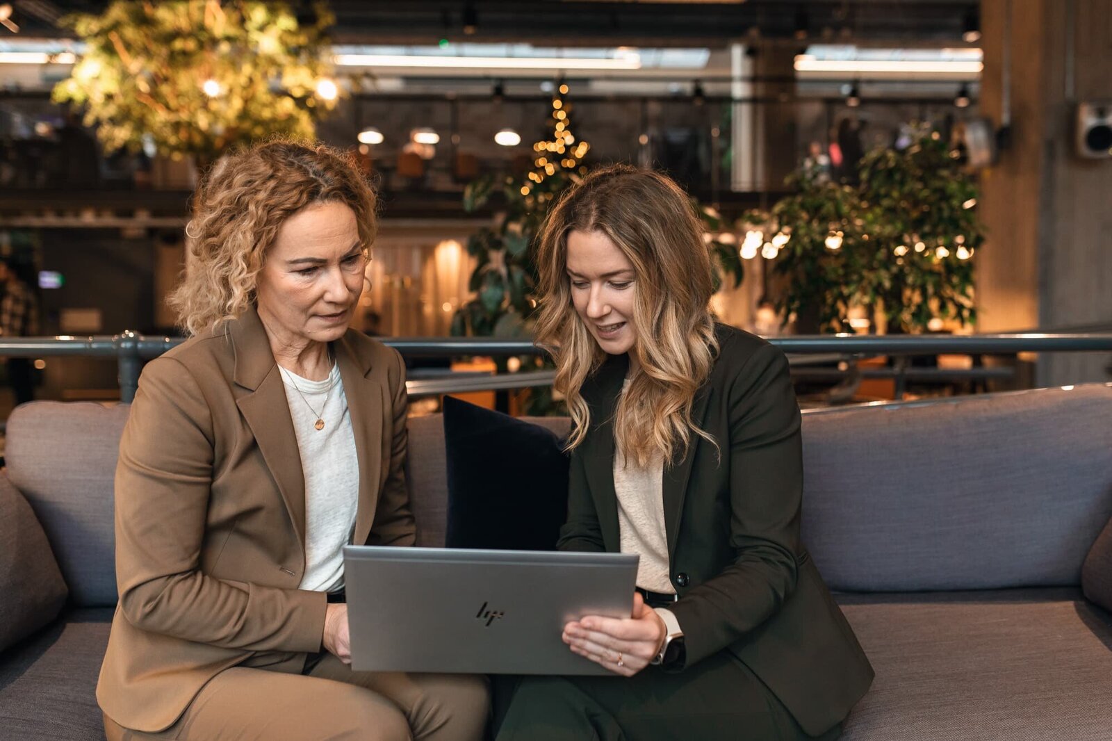 två kvinnliga företagare, med lockligt mörkblont hår, tittar på en dator.