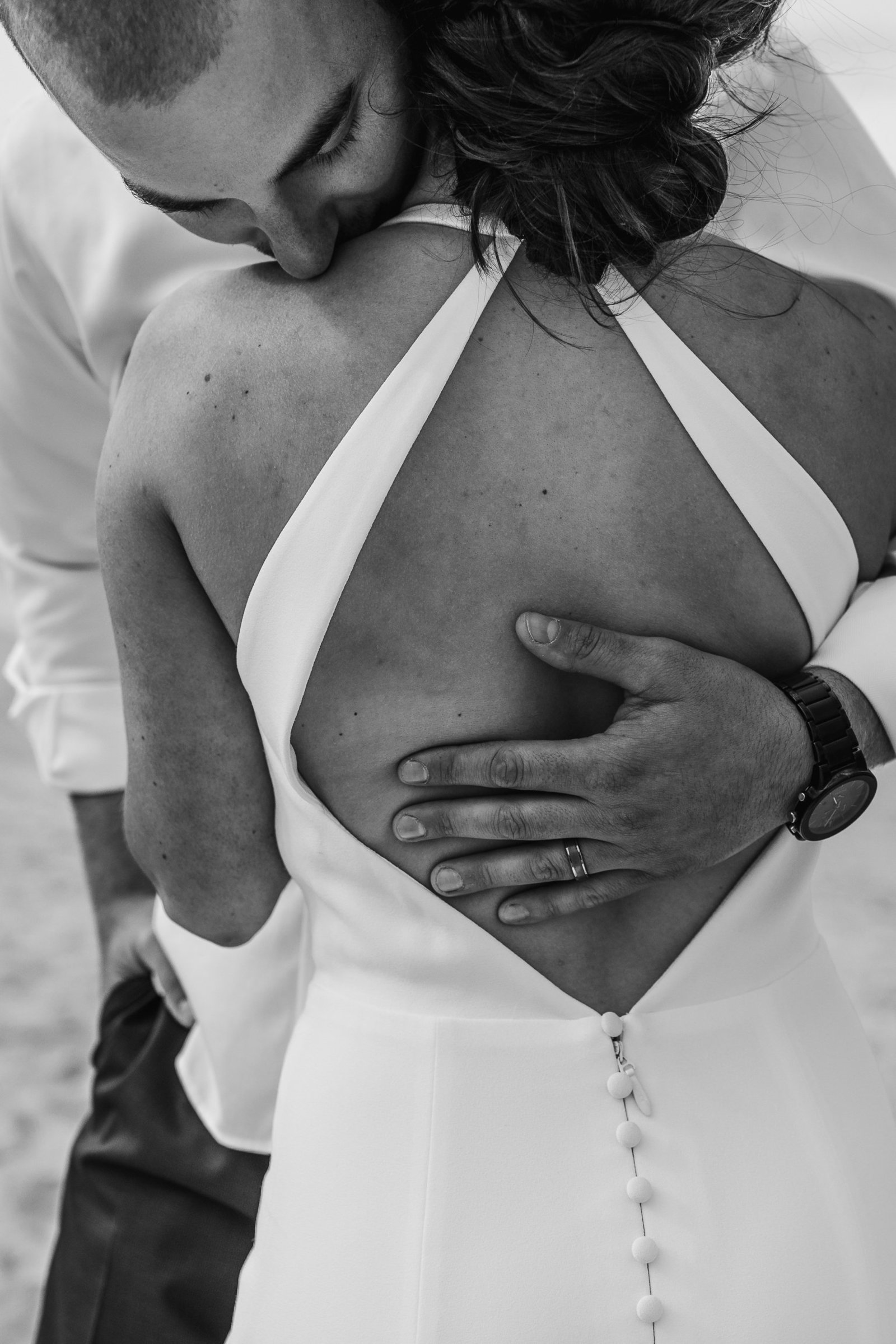 man kisses shoulder of his bride as he holds her close
