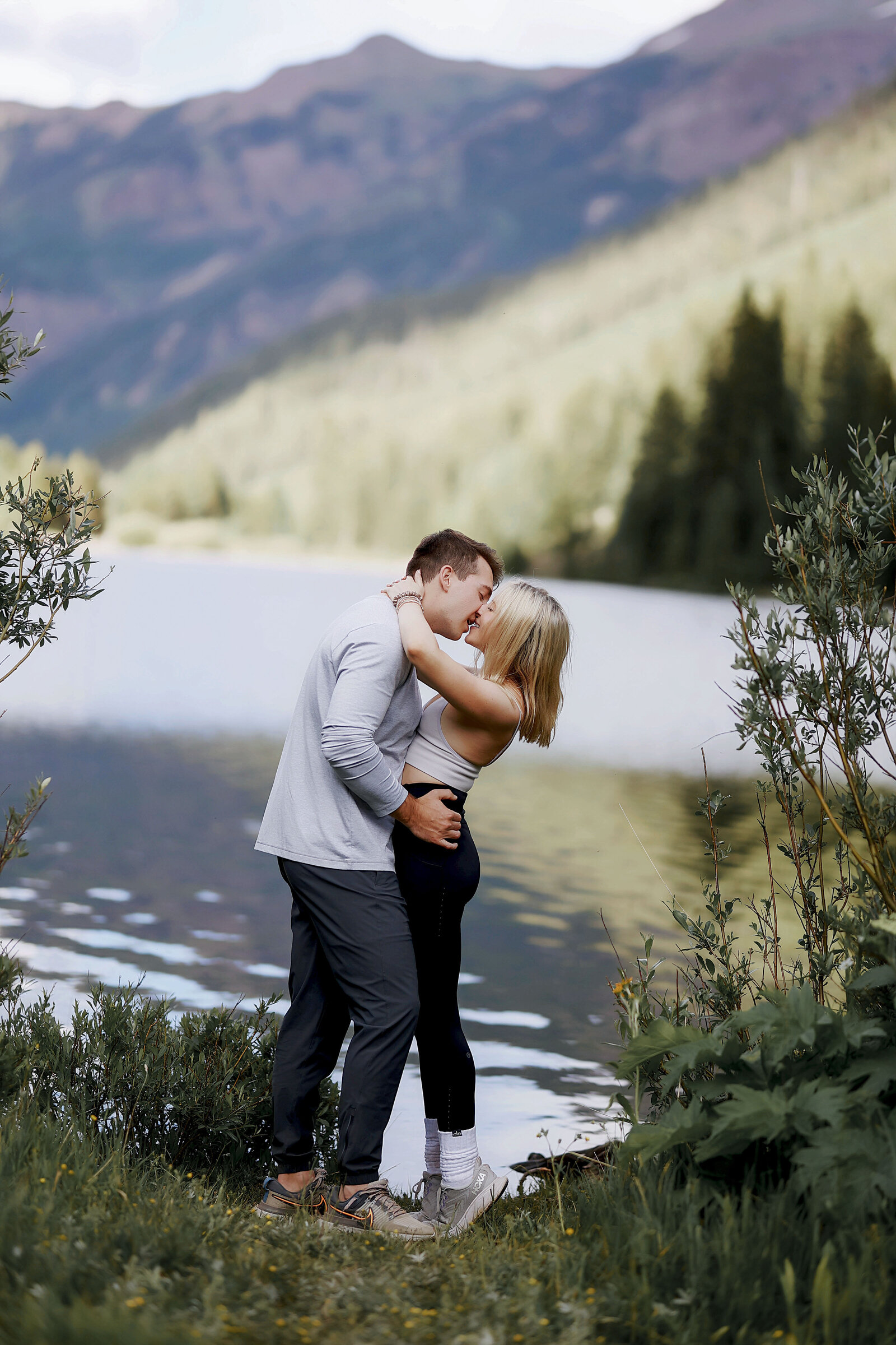 A beautiful couple hugs and kisses celebrating their engagement with the reflection coming off of Maroon Lake, at Maroon Bells in Aspen, Colorado,