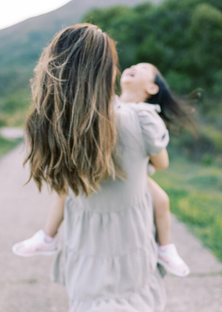 Backshot of mommy holding giggling daughter in the serene mountains.