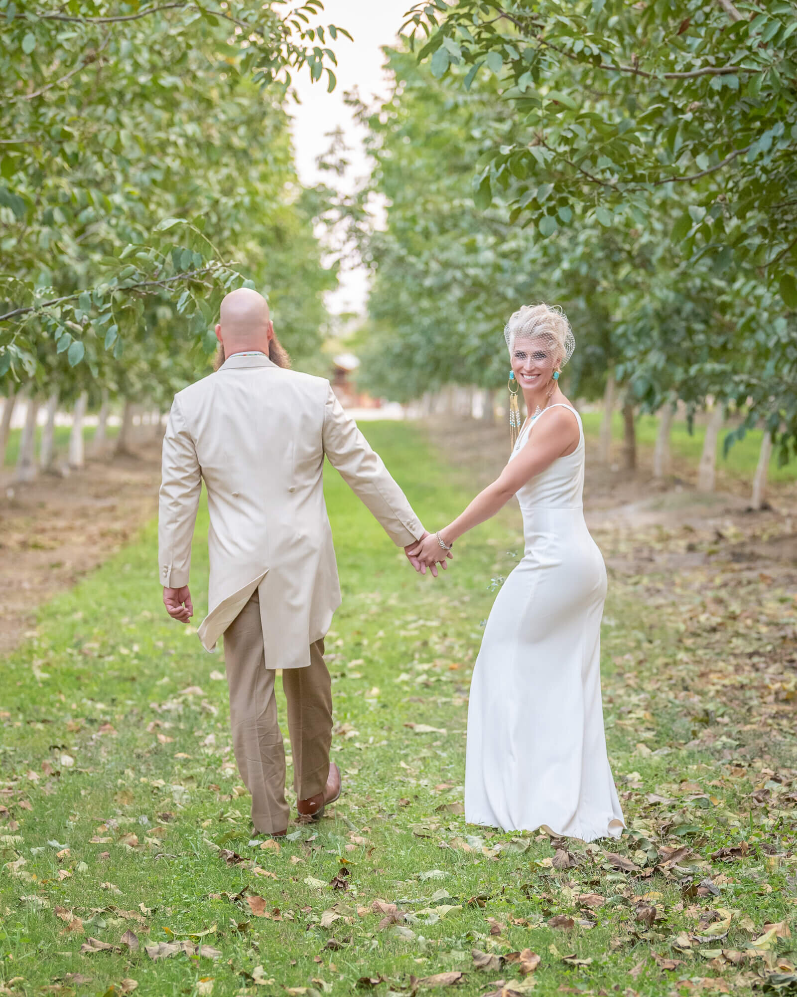 Bride and groom holding hands walking through an orchard