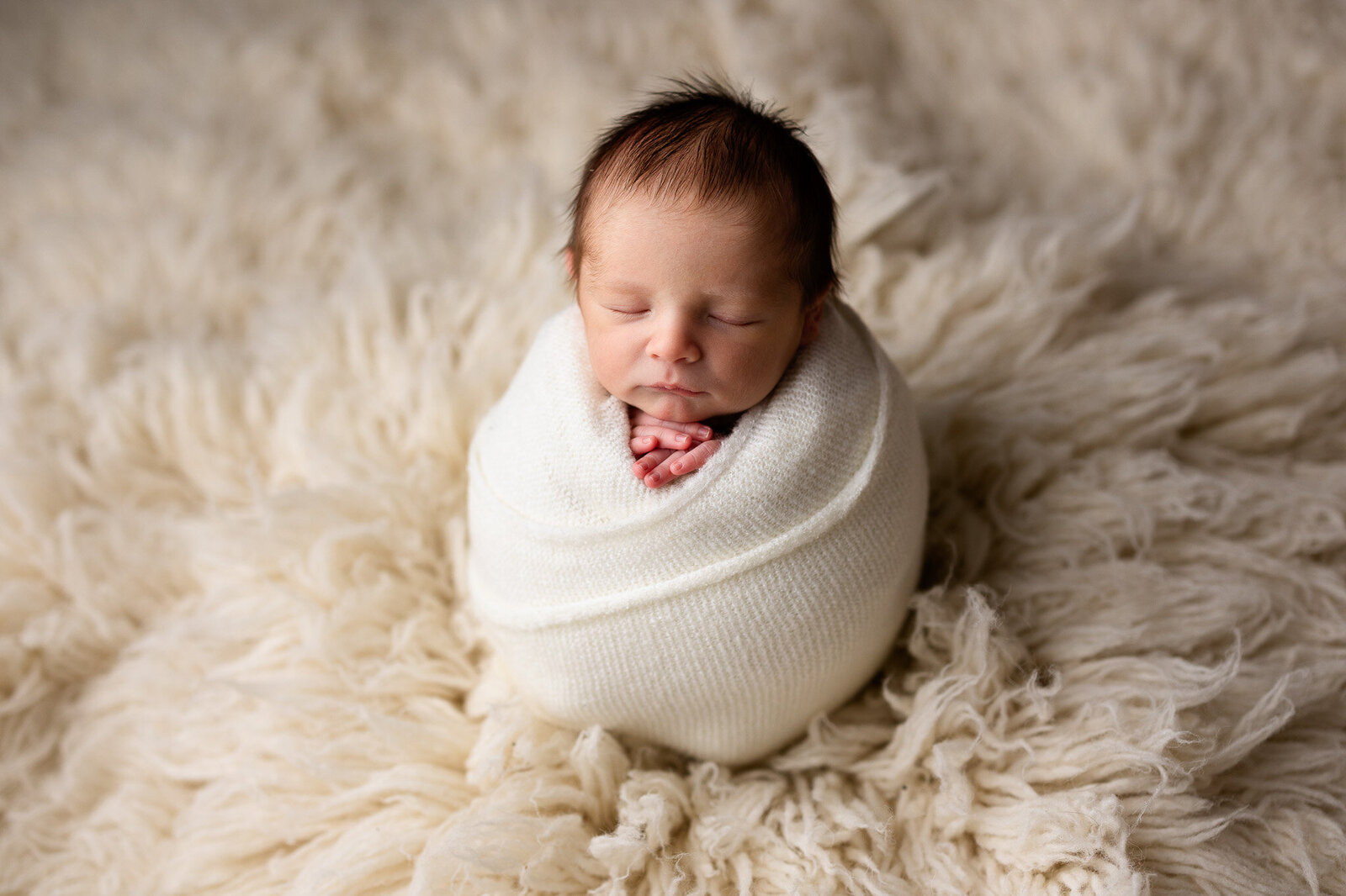 Baby boy wrapped in a cream wrap and posed upright on a cream flokati rug