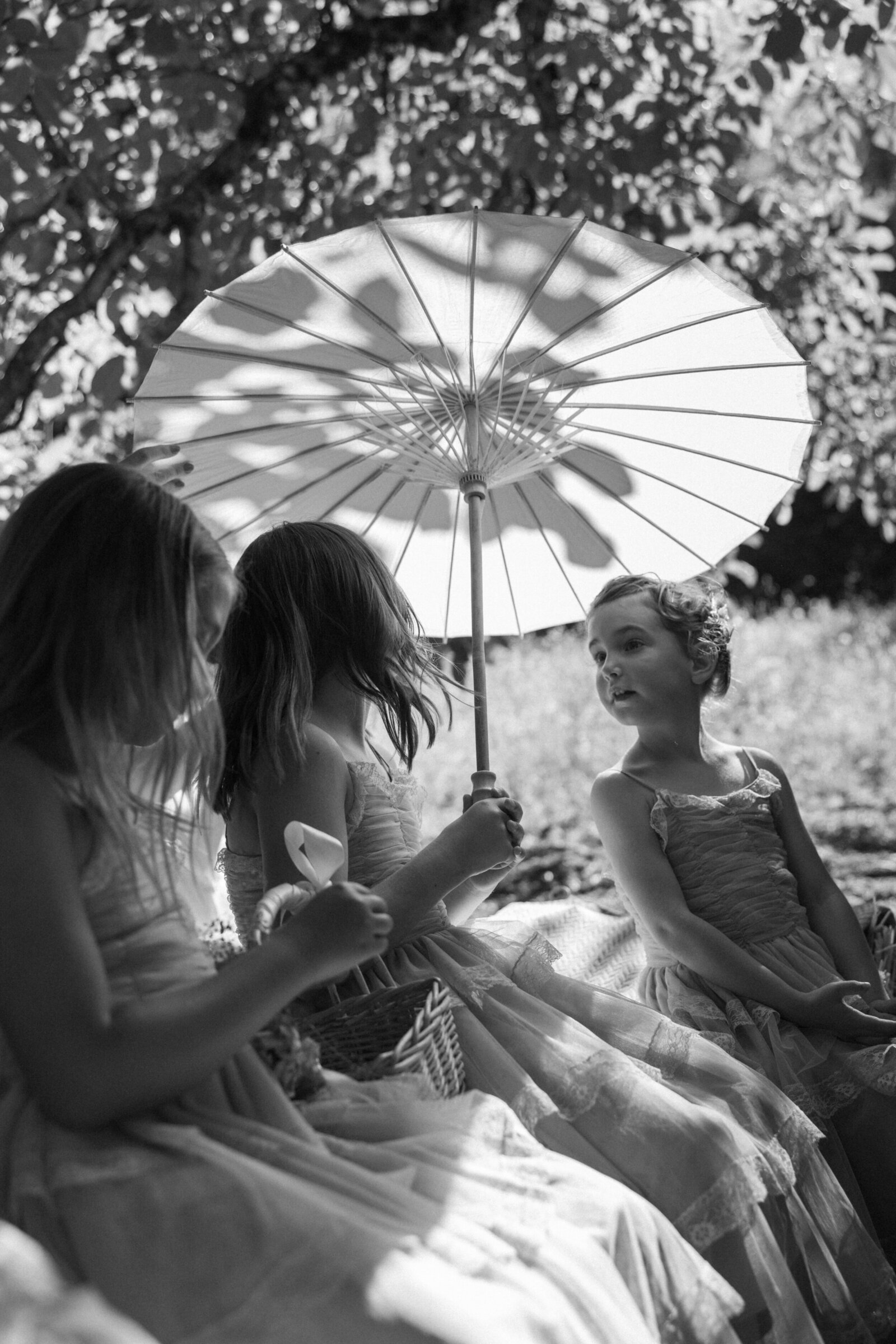 Candid black & white photo of flower girls holding parasol under ceremony tree during summer in Sonoma