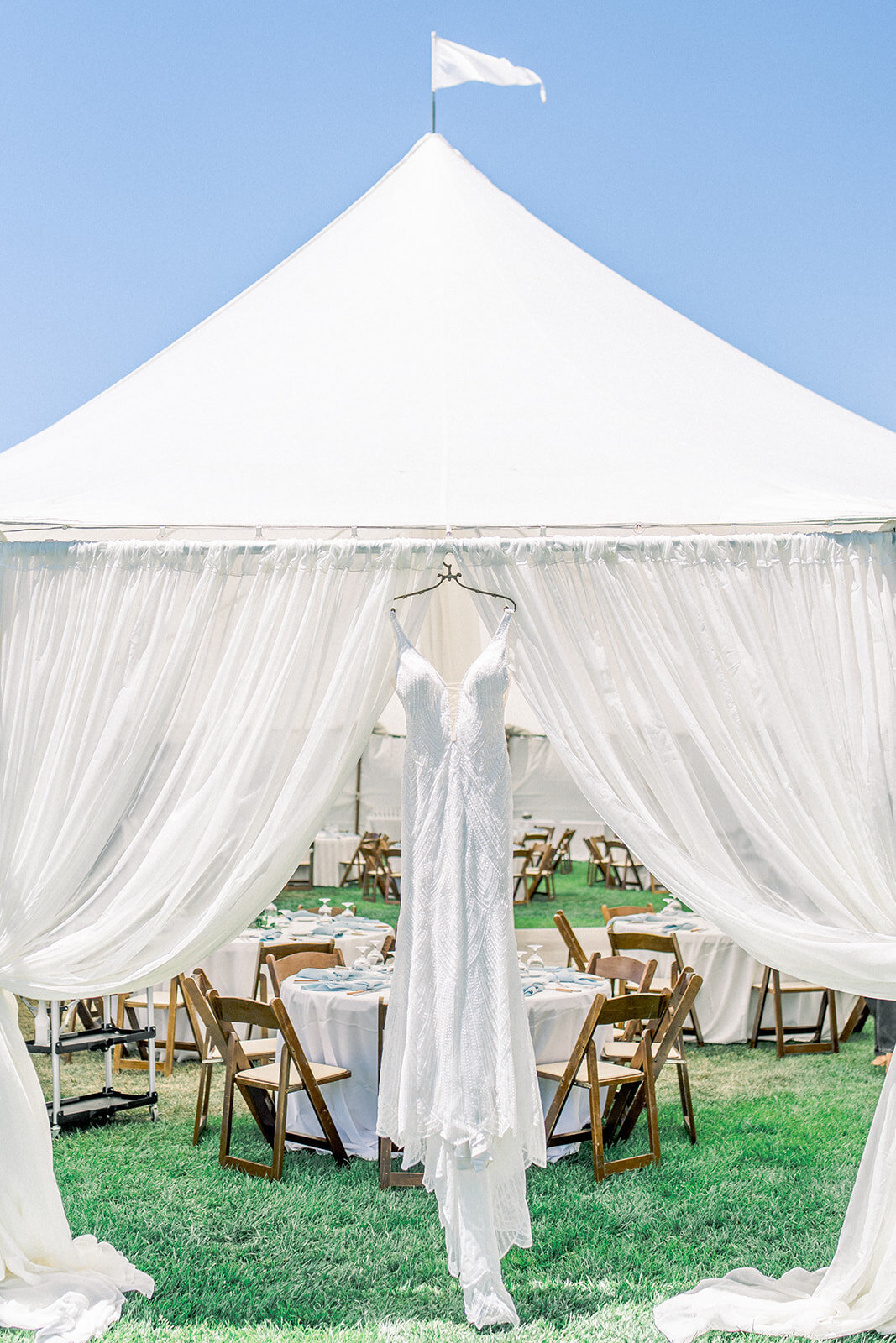 Wedding dress hanging on white reception tent at Dolphin Bay Resort in Pismo Beach, CA