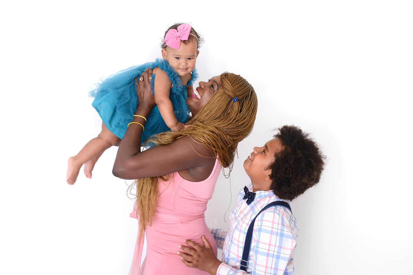 a mom lifts up her daughter in the air while her son looks at her and smiles