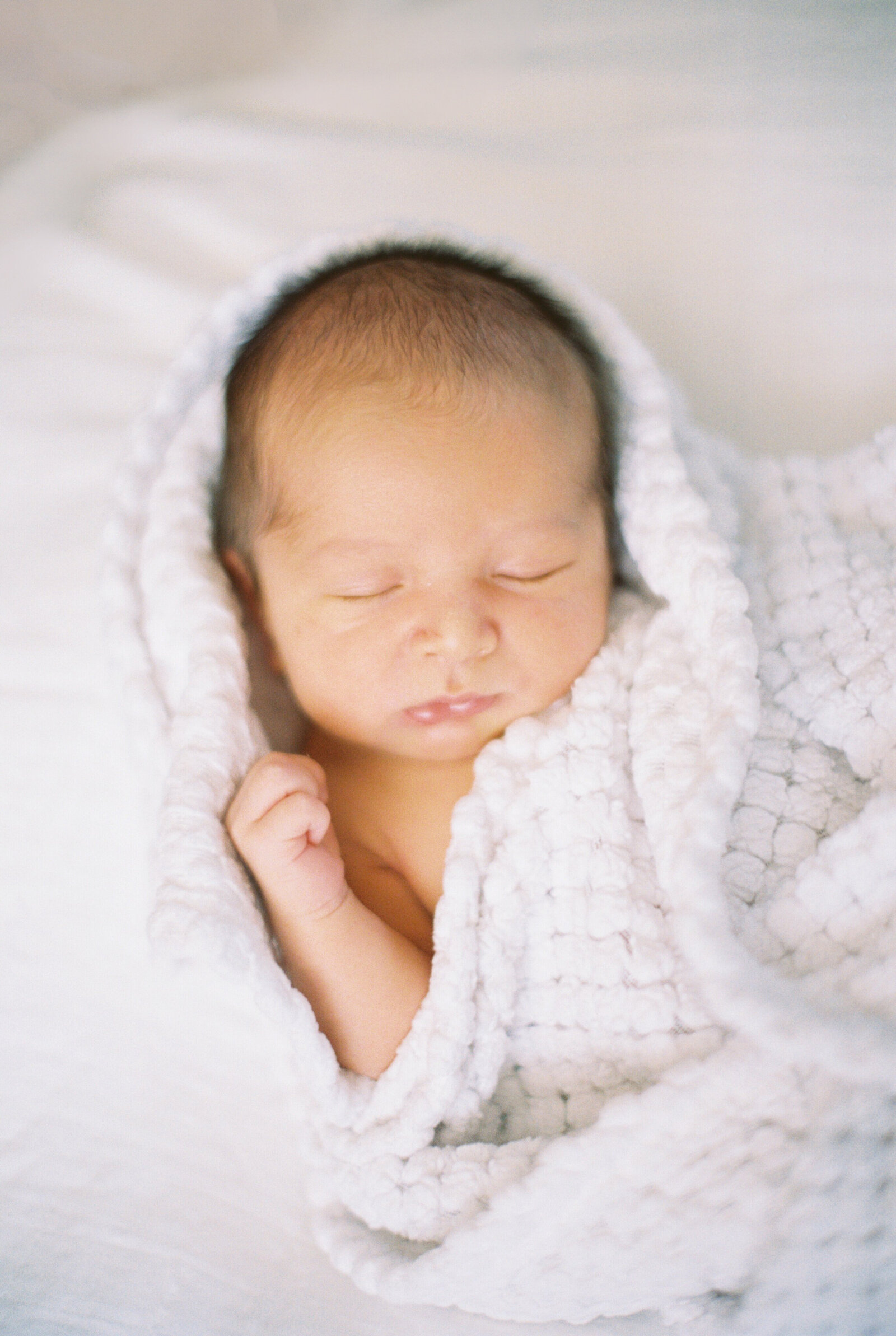 film image of a newborn baby wrapped in a white blanket sleeping