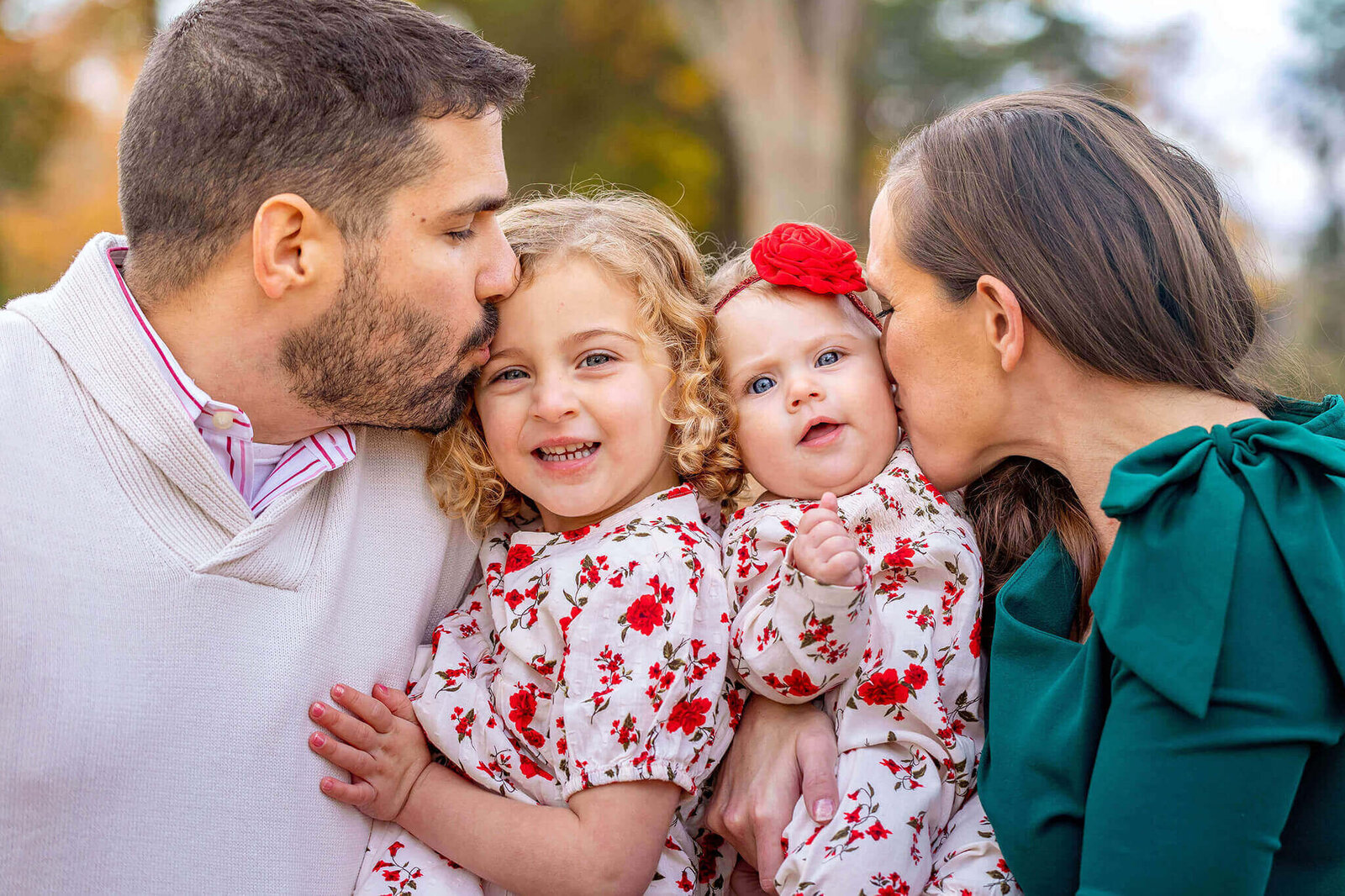 A mom and dad squeezing their two daughters between them and kissing them on the cheeks.