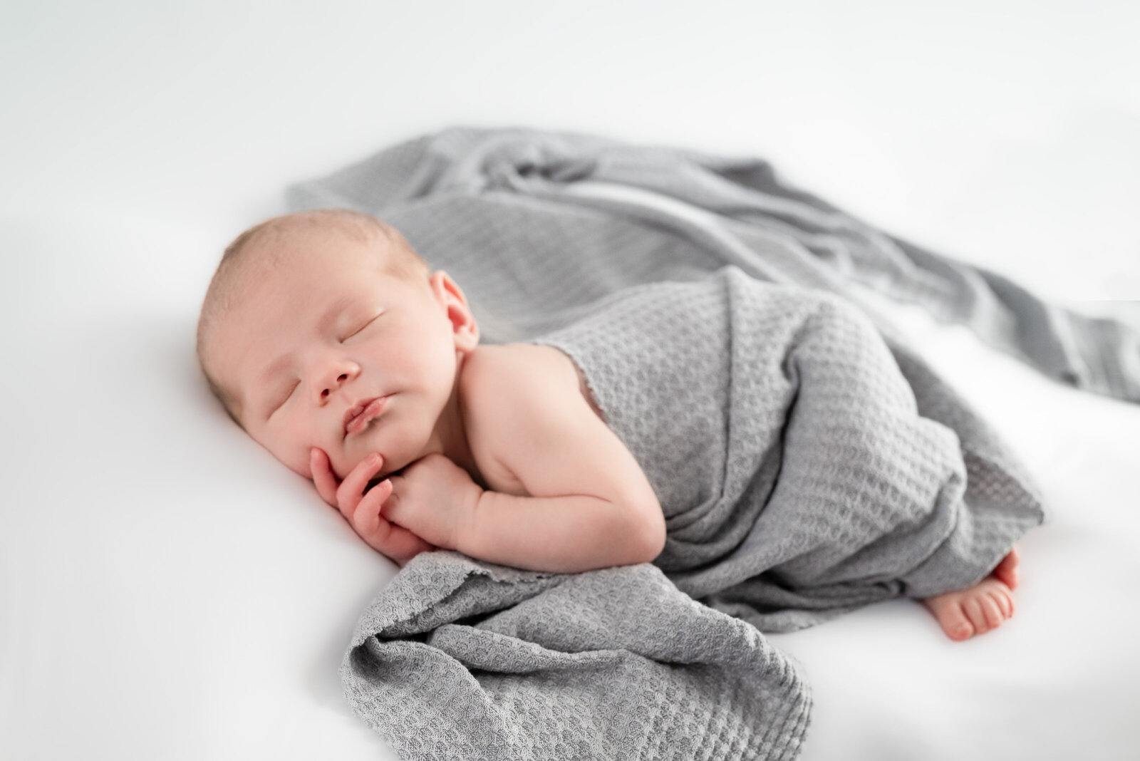 A newborn baby wrapped in a gray blanket and sleeping for his newborn photoshoot in Huntsville Alabama