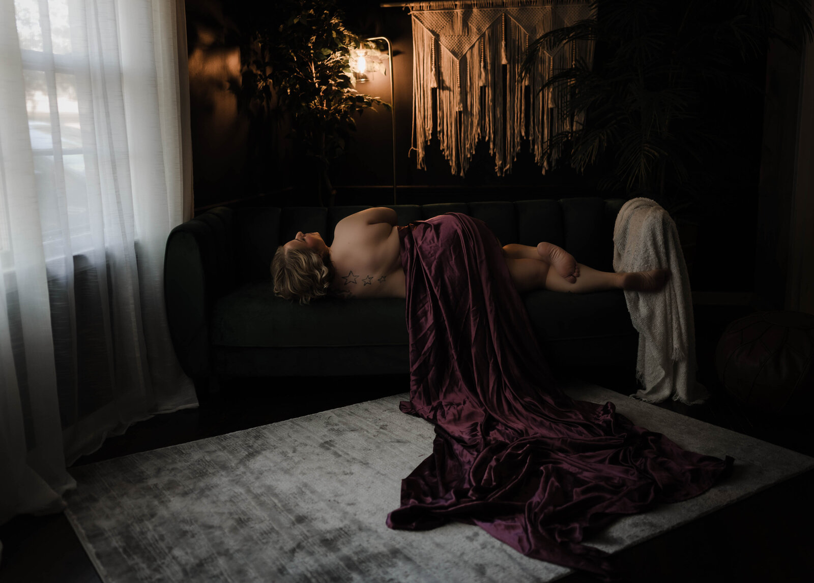 A woman sleeps on a couch under a purple sheet in a studio
