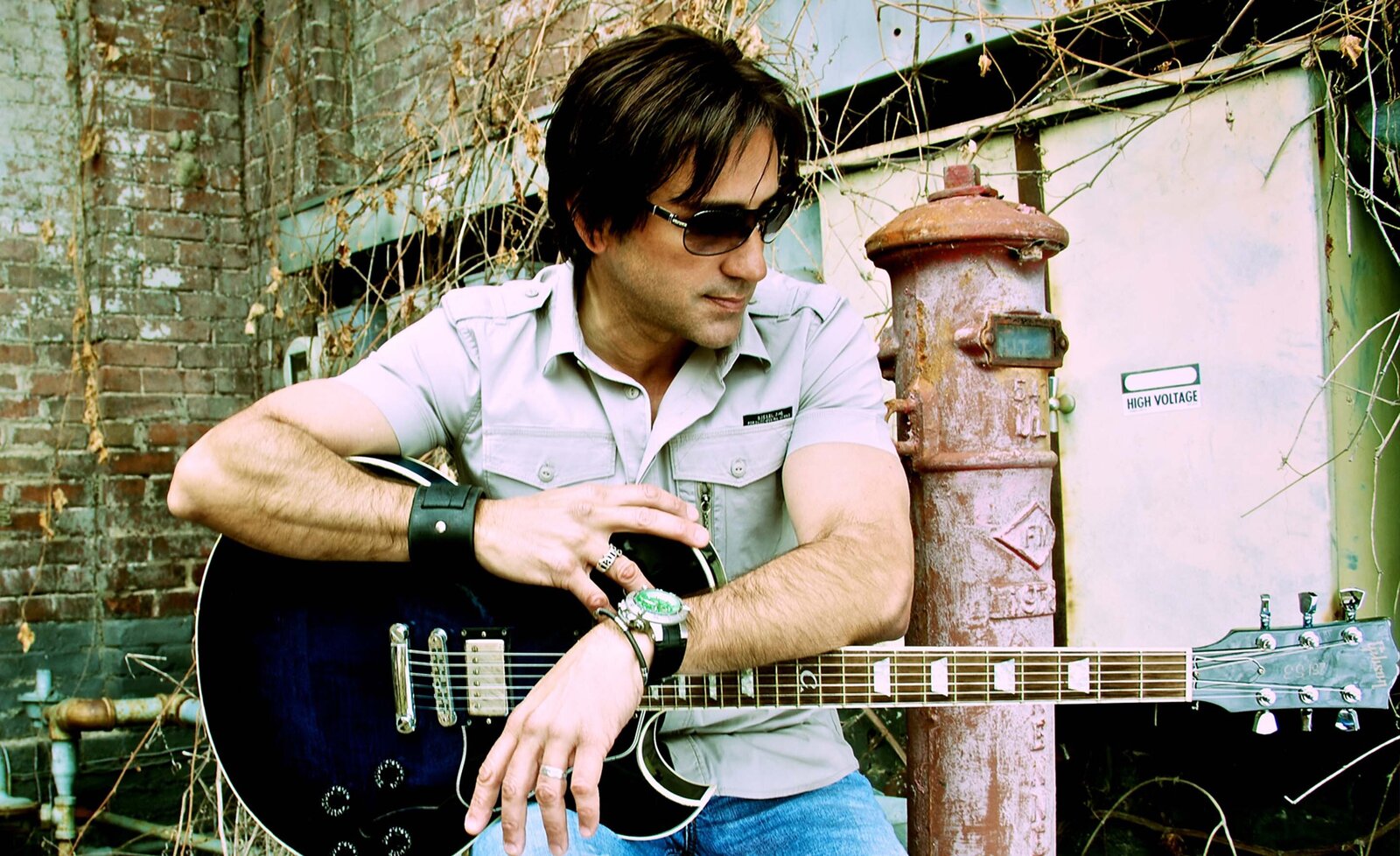 Steve Azar portrait sitting with black electric guitar wearing sunglasses in alley