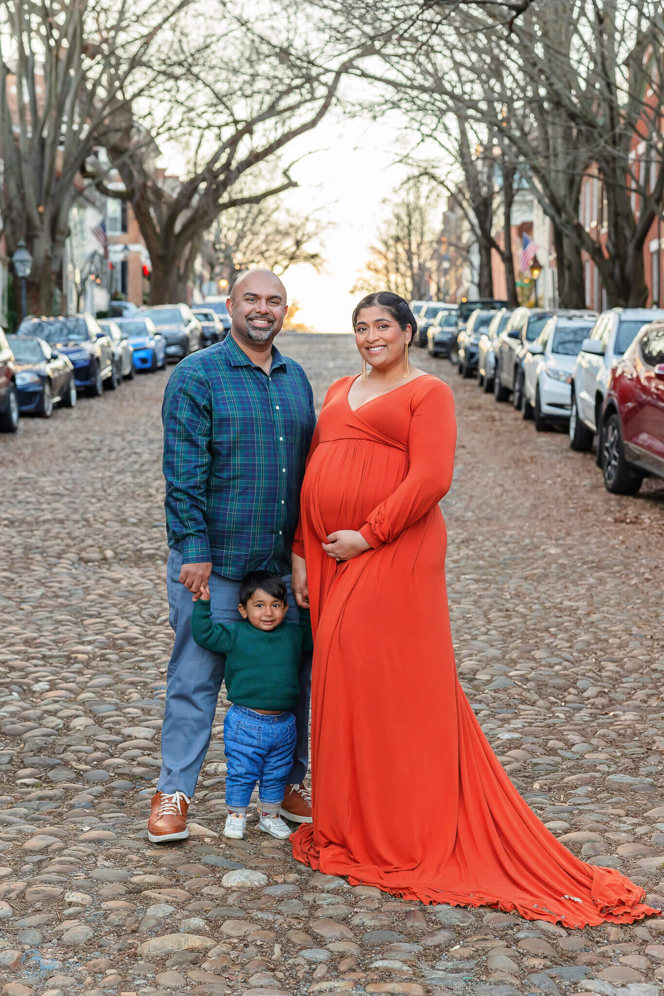 An expecting family posing on a cobblestone street in Alexandria.
