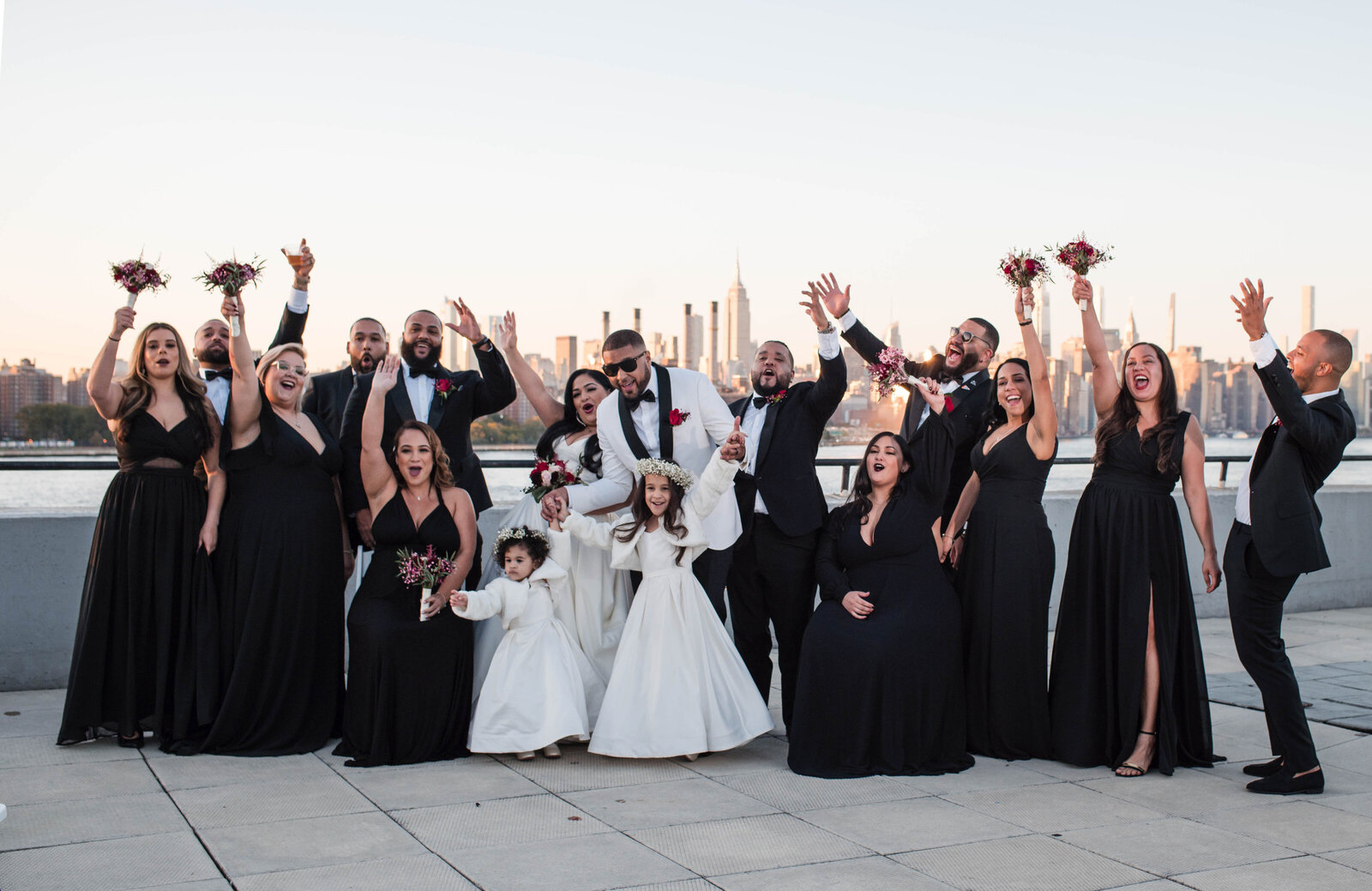 wedding party portrait - dressed in black bridesmaid dresses and black tuxedos in the W Loft  with the city skyline behnd them.