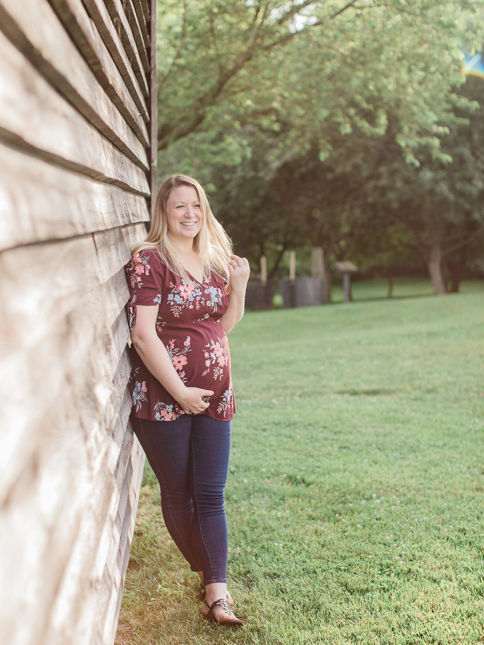 Blonde pregnant mother leans against a wall in red flower shirt, holding her baby bump