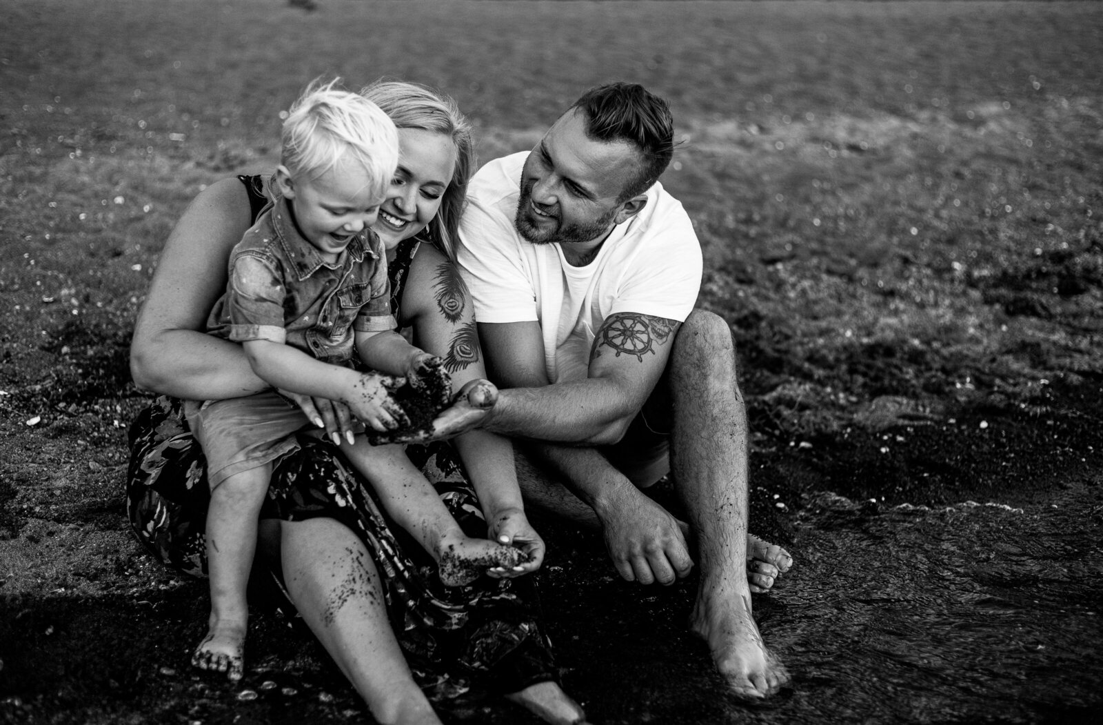 Black and white photo of family sitting on beach playing with sand.  Photo by Portland family photographer.