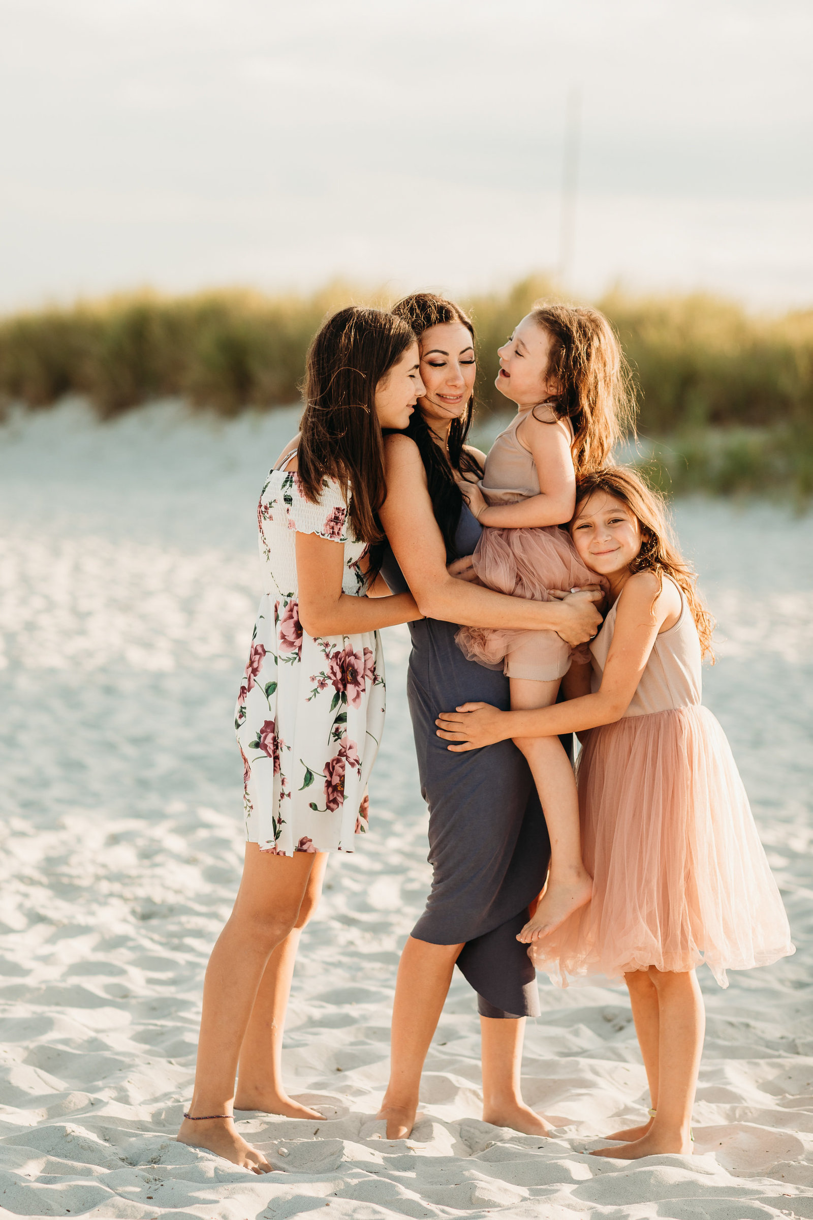 mother and daughters in dresses hug on a sandy beach in gloucester ma
