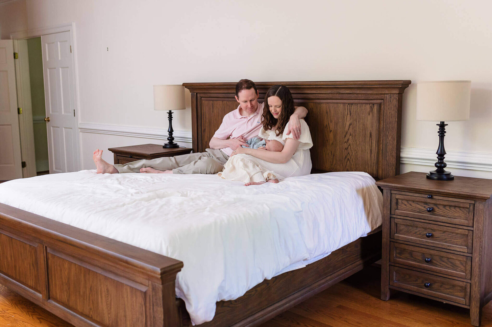 A mom and dad holding their newborn boy while sitting on their bed in their Northern Virginia home.