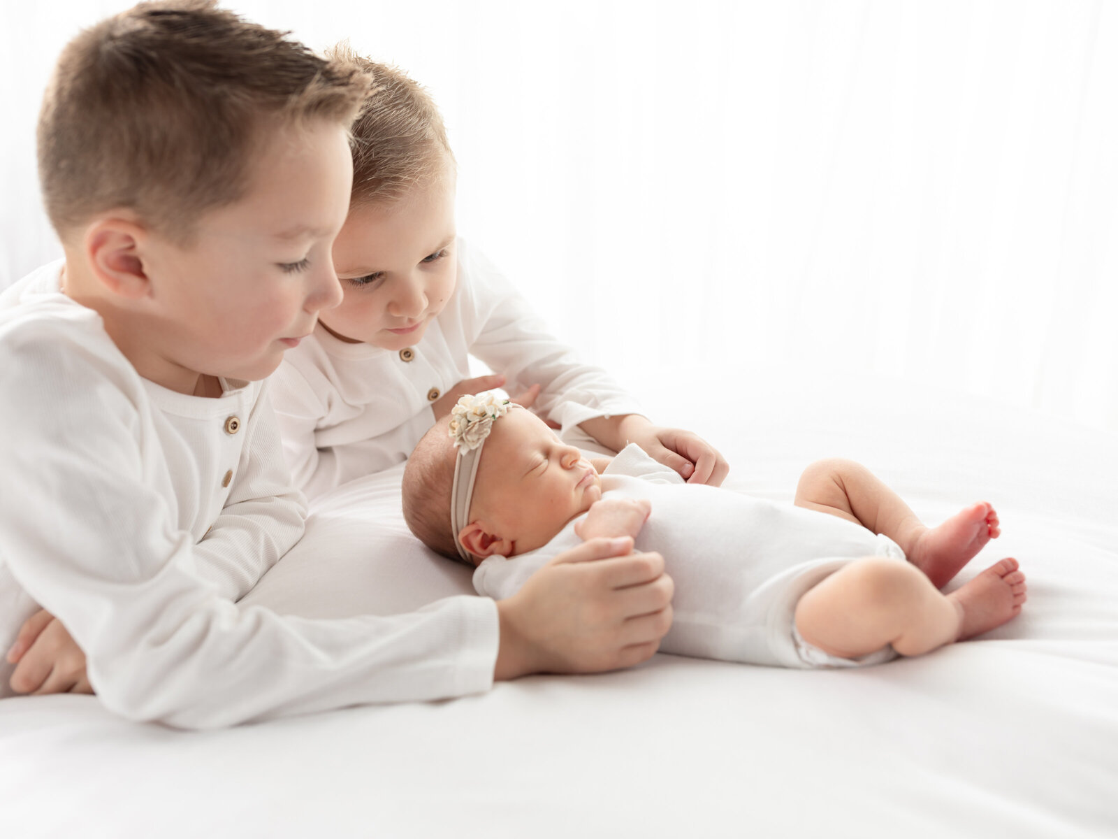 brothers looking at newborn baby sister on white studio set cleveland newborn photographer