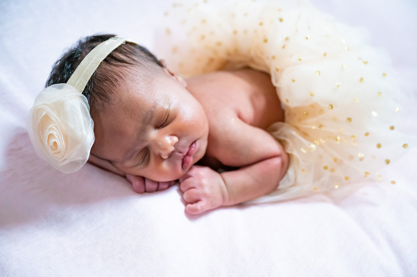 newborn baby girl with a white flower on her headband wearing a white tutu sleeping on a pink blanket photographed by Millz Photography in Greenville, SC