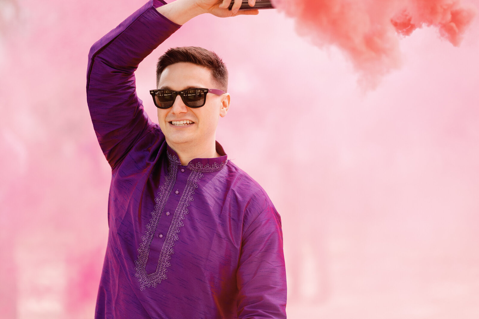 Groomsman with a colored smoke bomb, wearing sunglasses and a purple kurta during the Baraat