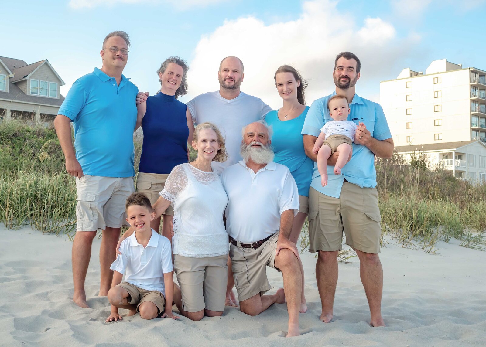 A family gathers near the beachfront homes at Wrightsville Beach, dressed in white and blue attire. With smiles and a relaxed pose, they capture the essence of a coastal family vacation. Perfect for professional family photography in NC, showcasing beachside elegance.