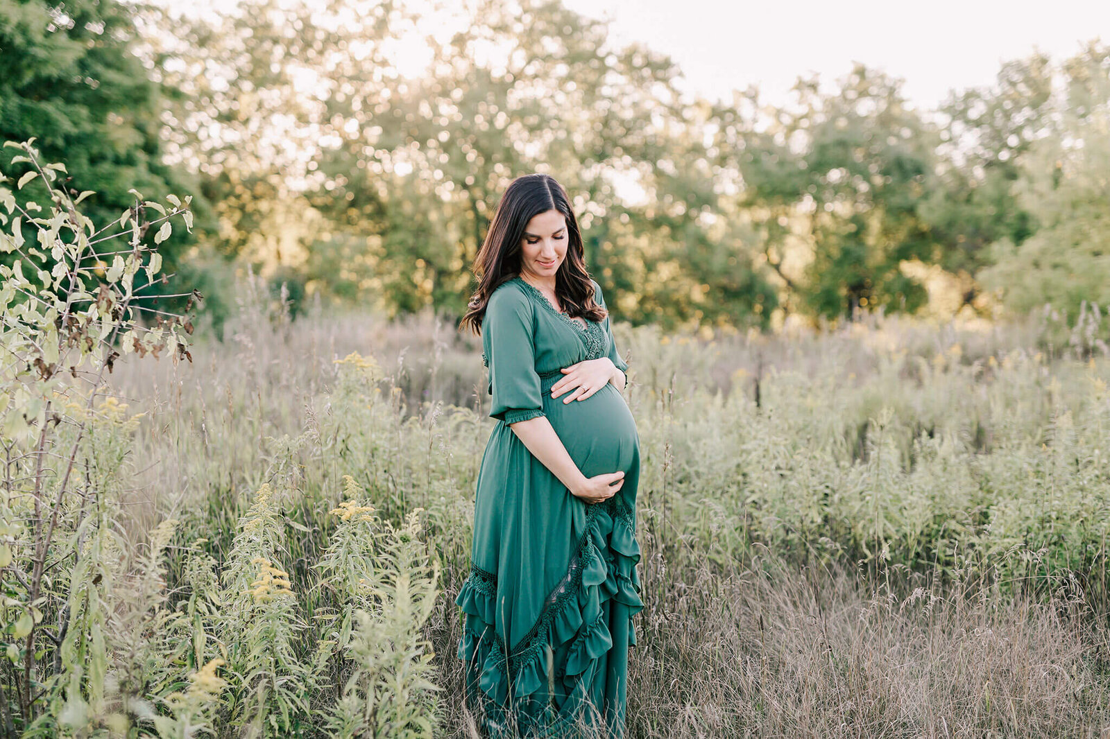 Mother to be in a green Baltic Born dress wholes her baby belly with with both hands.