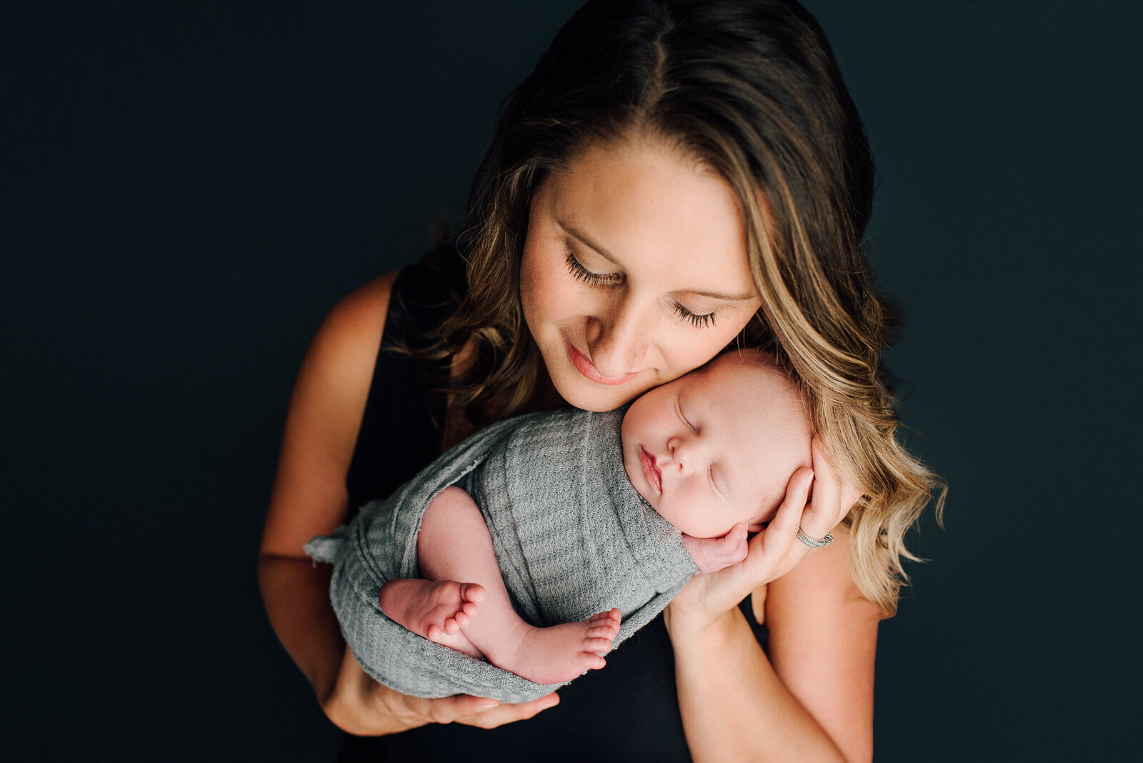 In home studio newborn photo of mom holding baby with dark background in Jacksonville, FL.