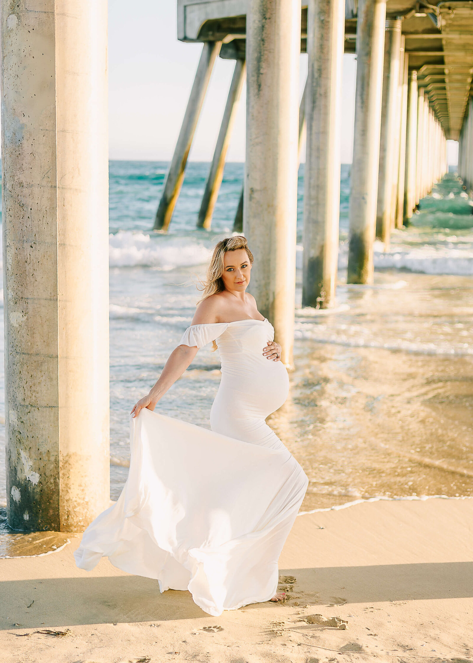 Mom holding dress during maternity session at Huntington Beach Pier.
