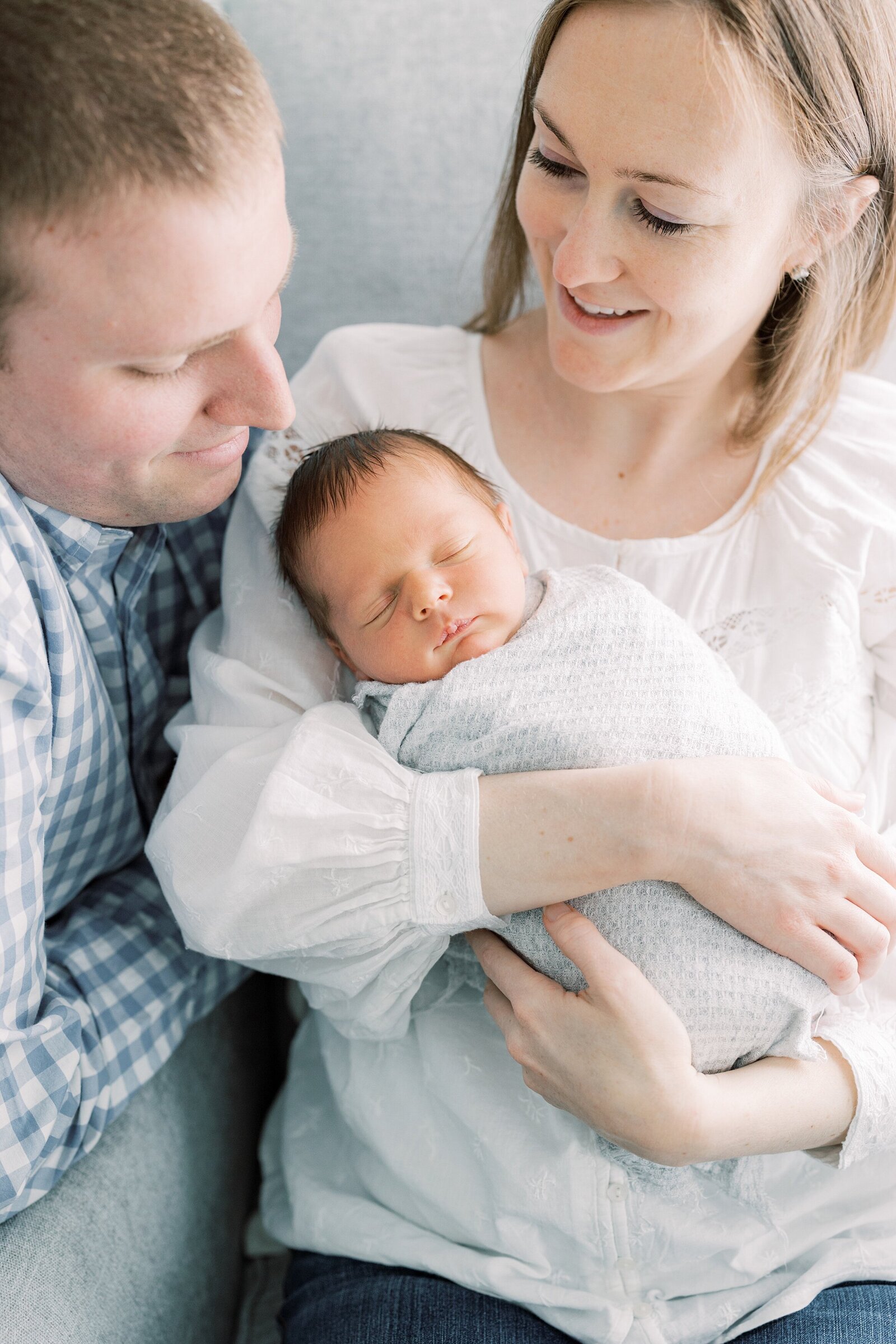 mom holding sleeping baby while dad looks on Newborn Photography West Chester PA