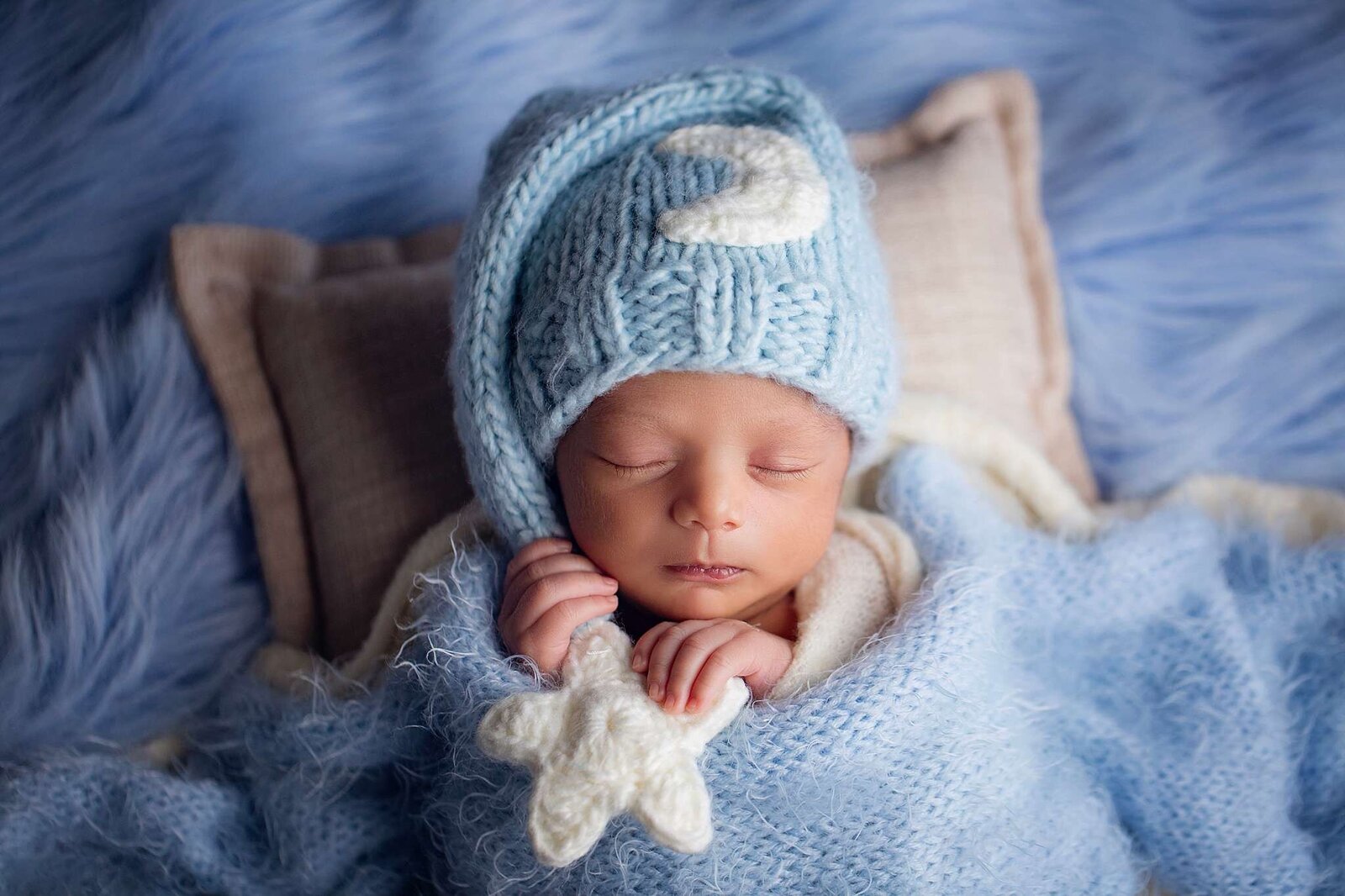 Newborn boy with a knitted hat and blue blanket, photographed by Bia Schaefer during an in-home newborn session in Orlando, Florida.