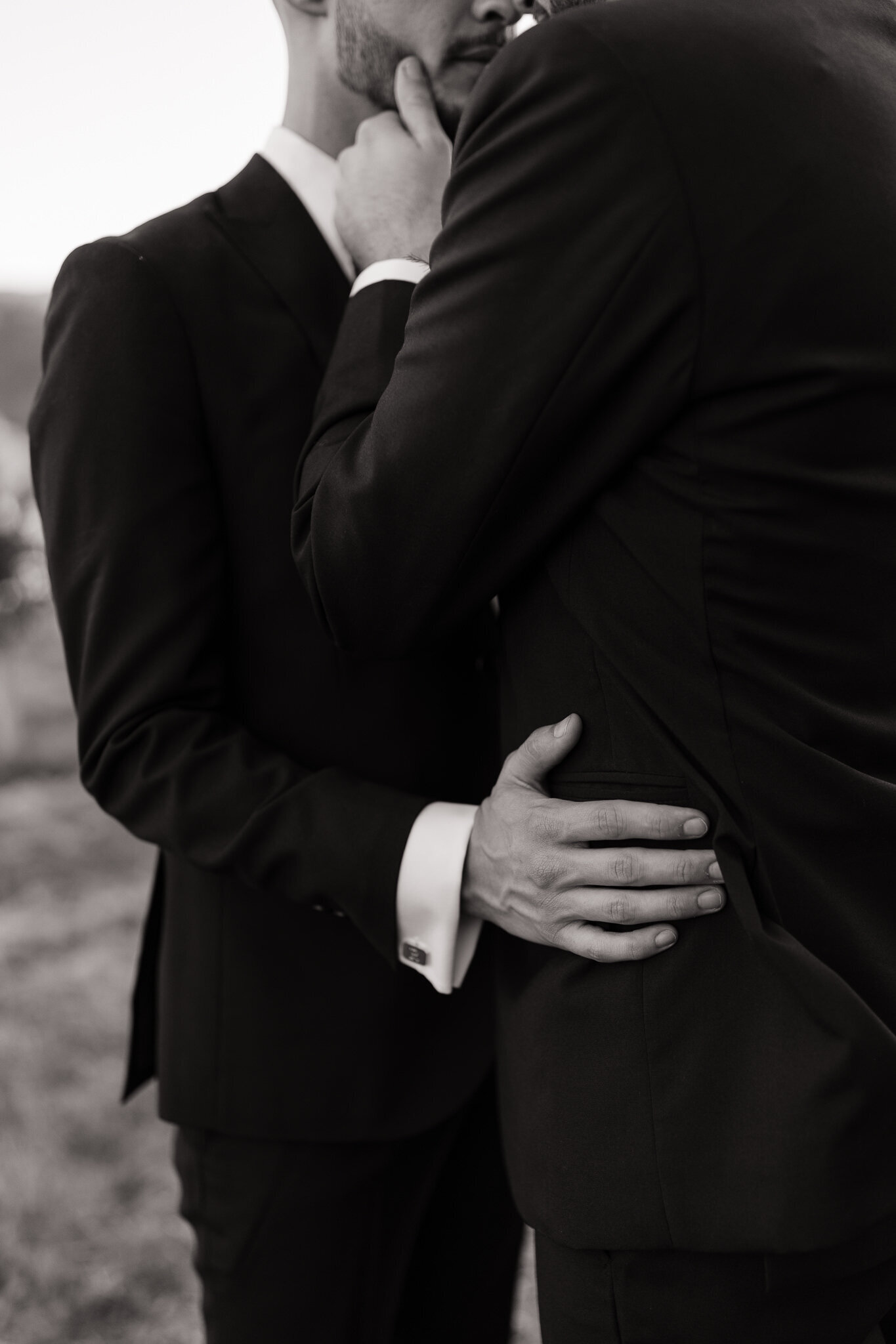 Close up of grooms embracing with vineyard backdrop at Nelson Family Vineyards wedding venue