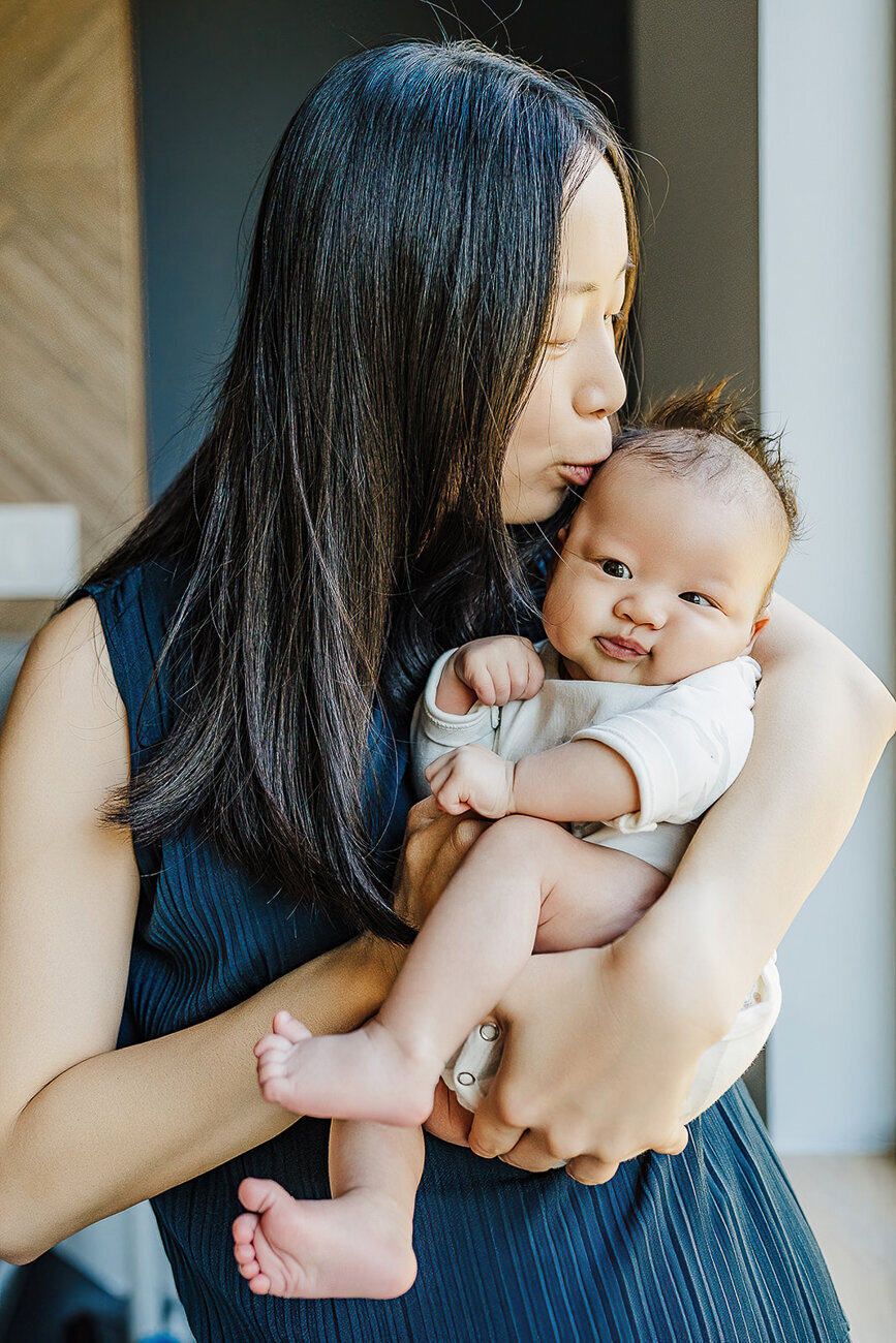 mother kisses newborn baby boy with chubby cheeks