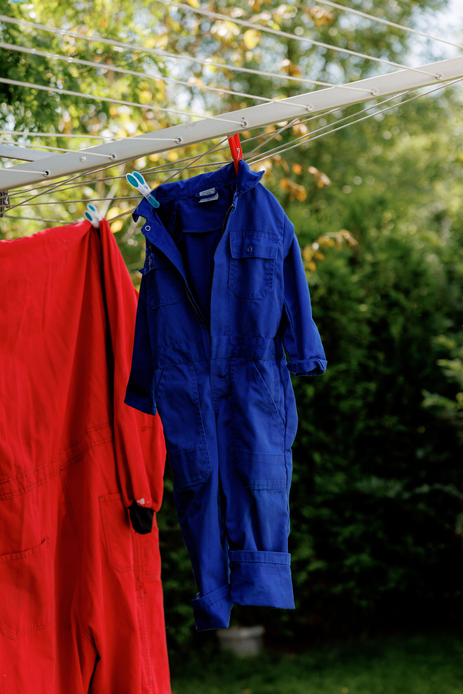 Blauwe en rode overalls hangen aan de waslijn in de tuin bij Kinderdagverblijf Bij Ons Op De Boerderij.