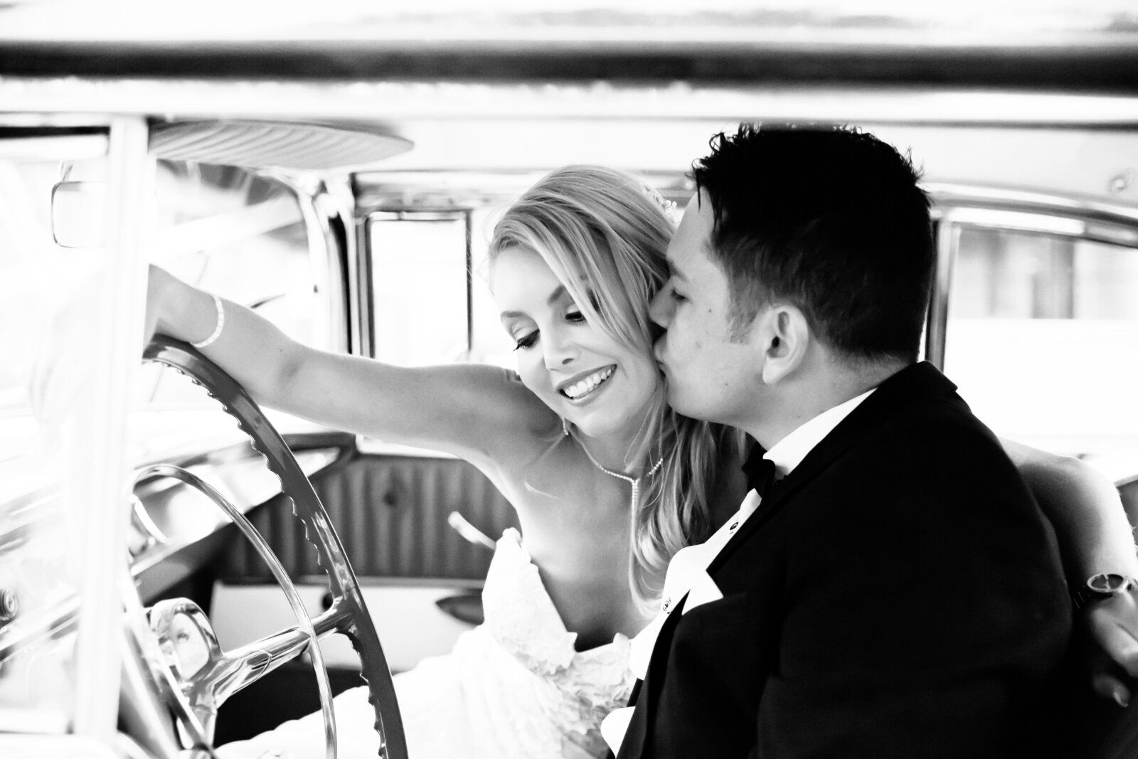 groom kisses glamorour bride in car in black and white