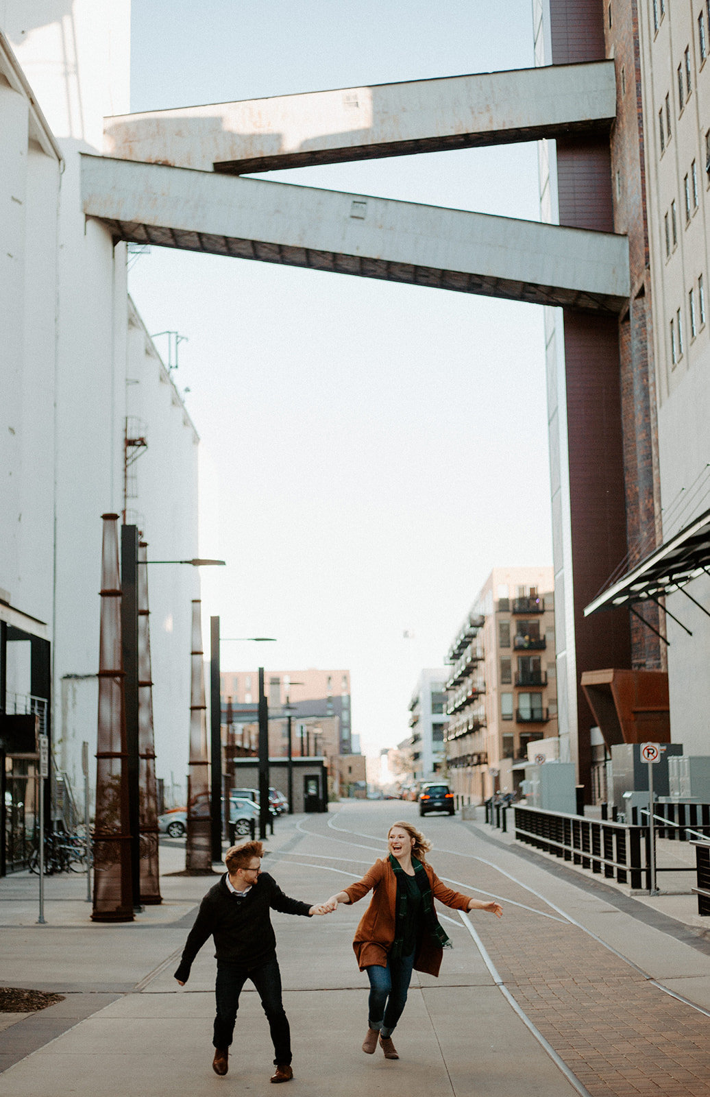 Couple holding hands running down a street in downtown Minneapolis during their engagement session