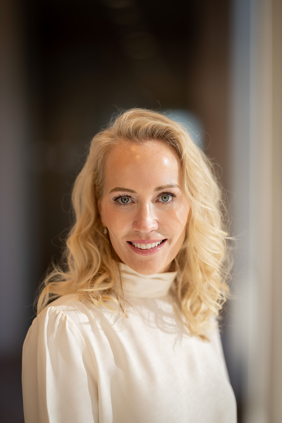 Elegant portrait of a woman in a white blouse, glowing with soft natural light.