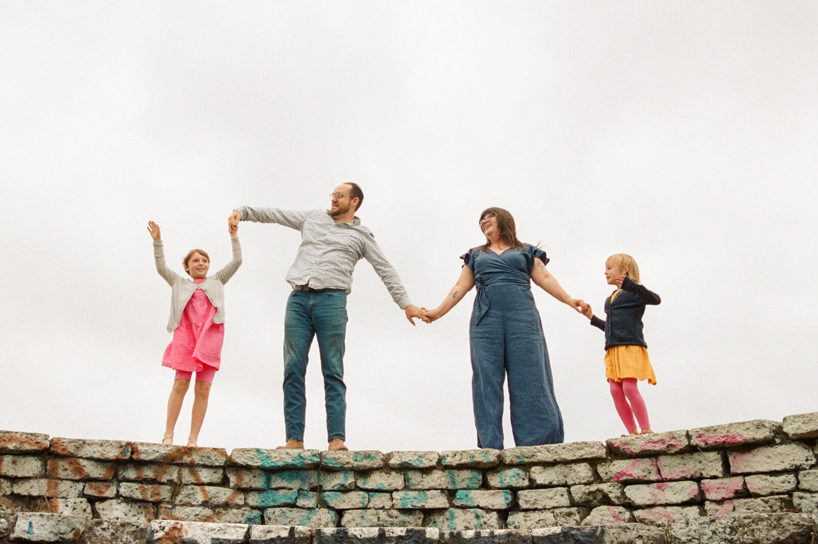 photo of family of four standing on stone wall holding hands