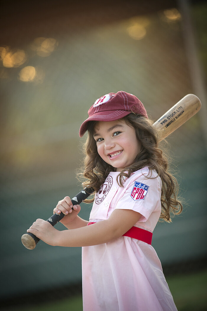 Young girl posing with baseball bat smiling big.