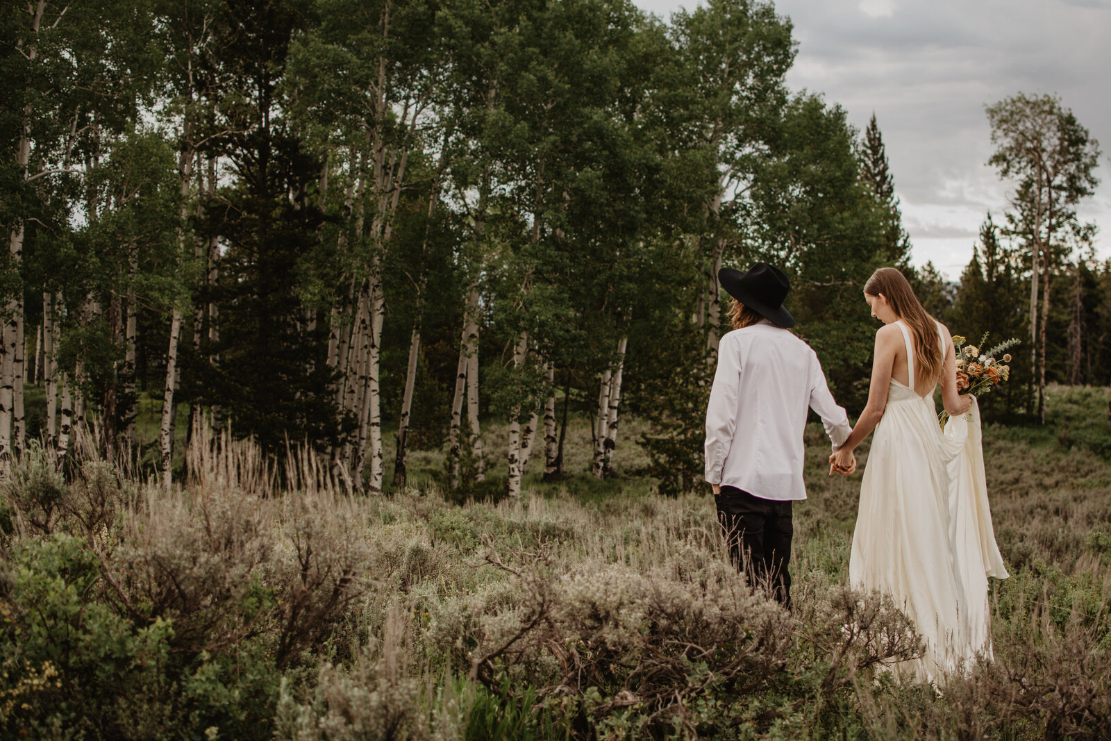 forest wedding in the grand tetons with bride and groom holding hands and walking together into the woods for a jackson hole wedding