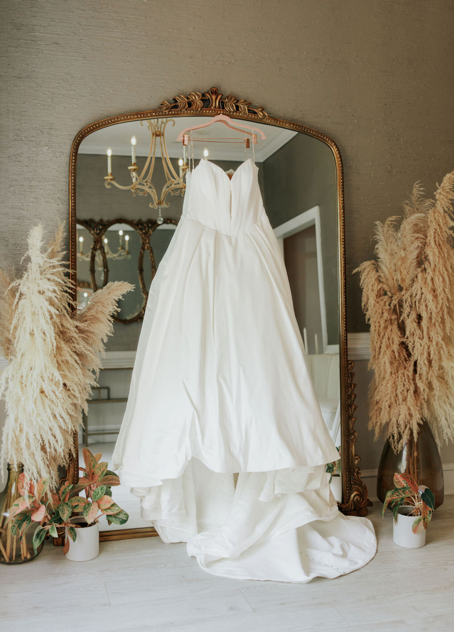 White wedding dress hanging on mirror with pampas grass decor