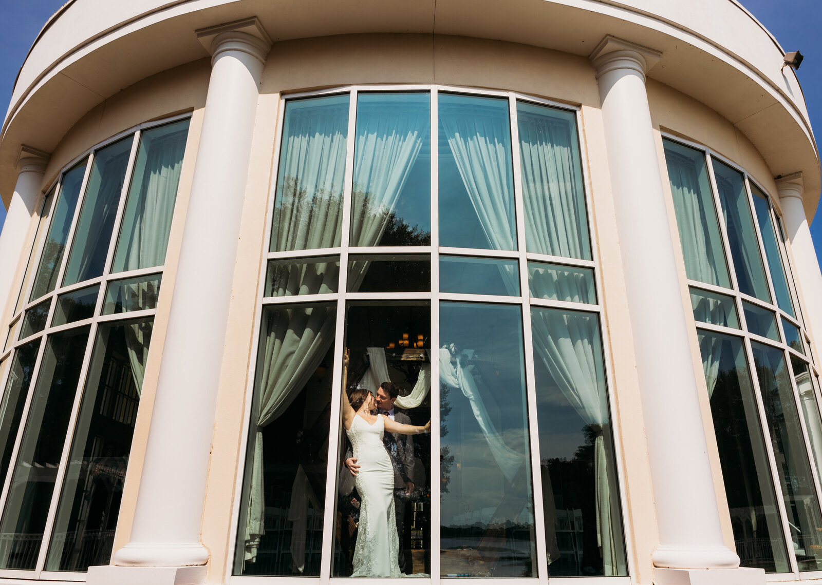 Newlyweds pose through massive windows at Lake Mary Event Center, their reflection captured in the glass during a Florida wedding session.